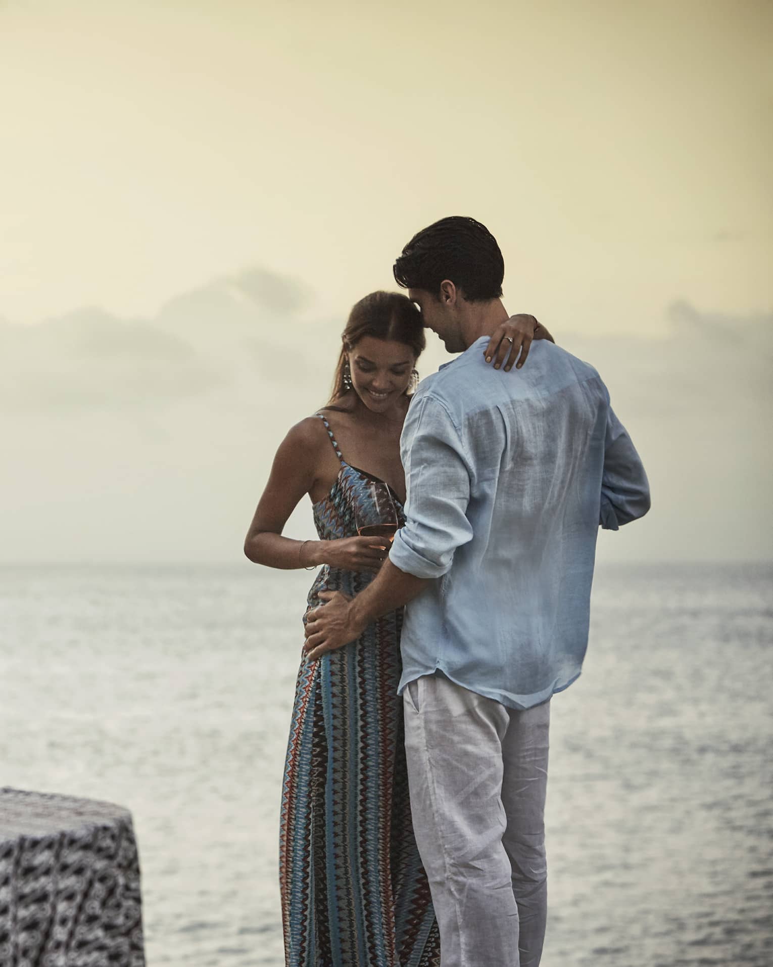 Couple embraces beside private dining table overlooking ocean at sunset