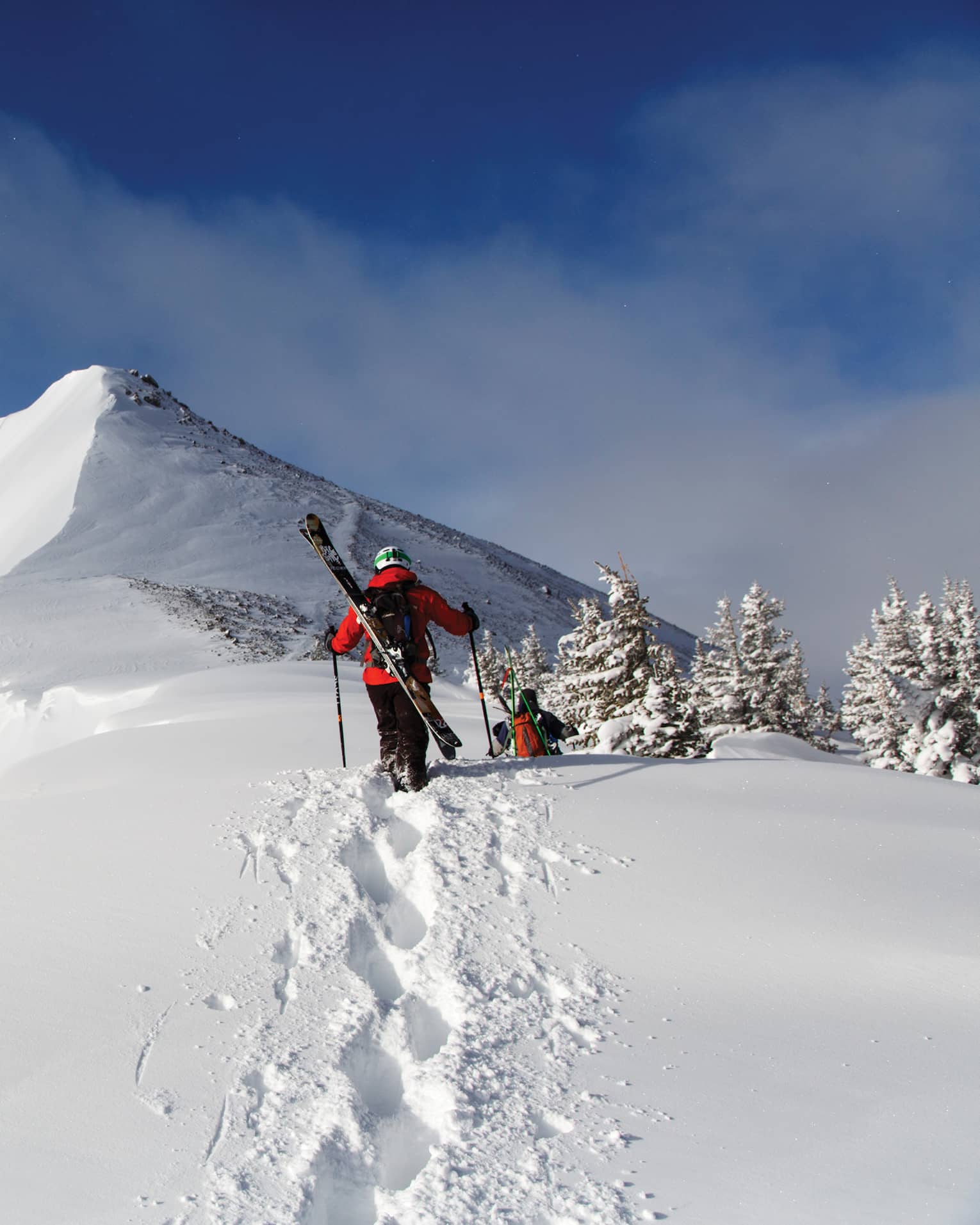 Two people with skis on their backs walking in snow.