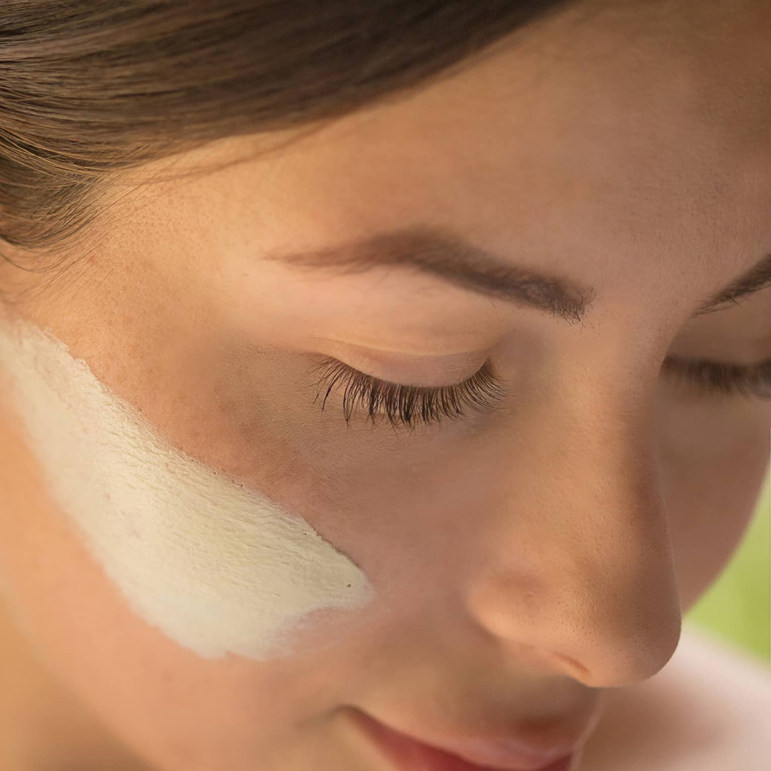 Close-up of side of woman's face with lotion on cheek