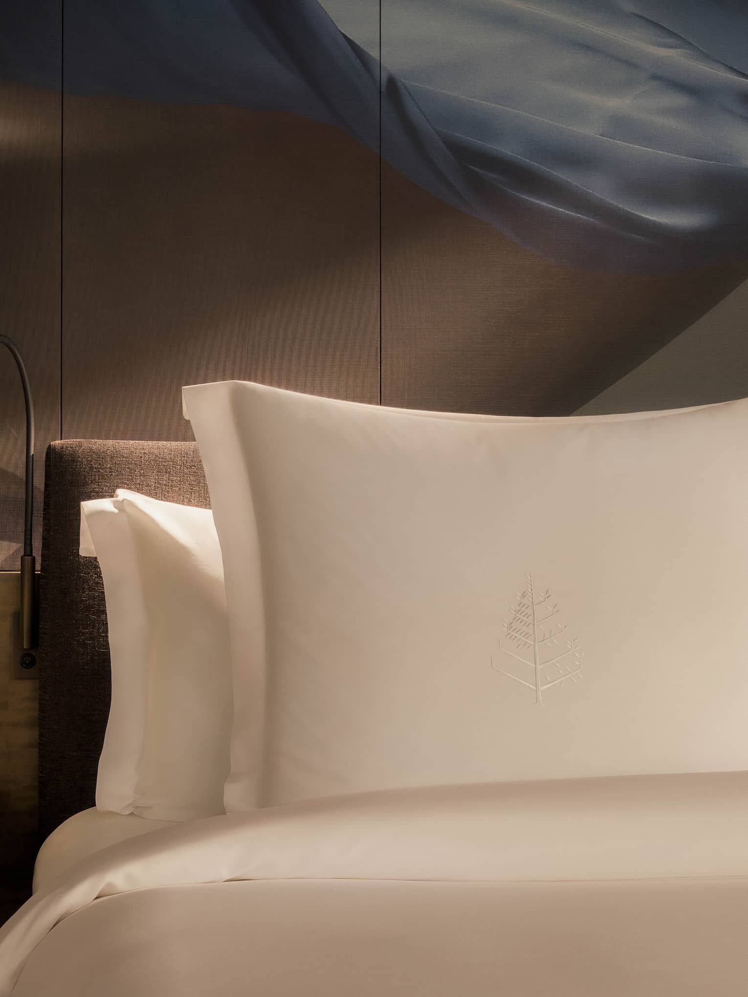 Luxury hotel room bed with artistic accent wall behind white pillows and sheets, and a wooden side table with flowers