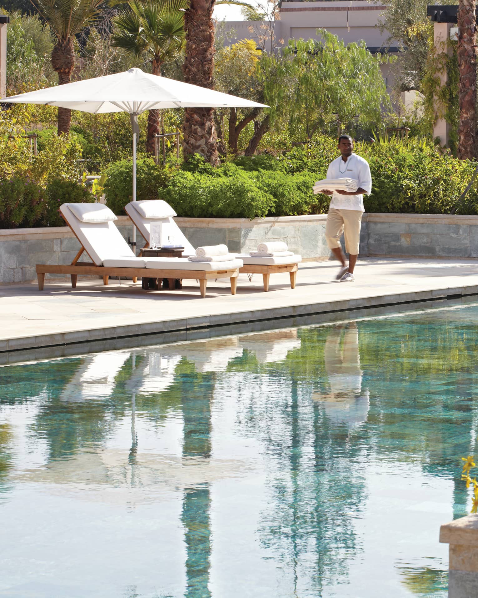 Server holding folded towels walks by lounge chairs, umbrella by adults-only outdoor swimming pool