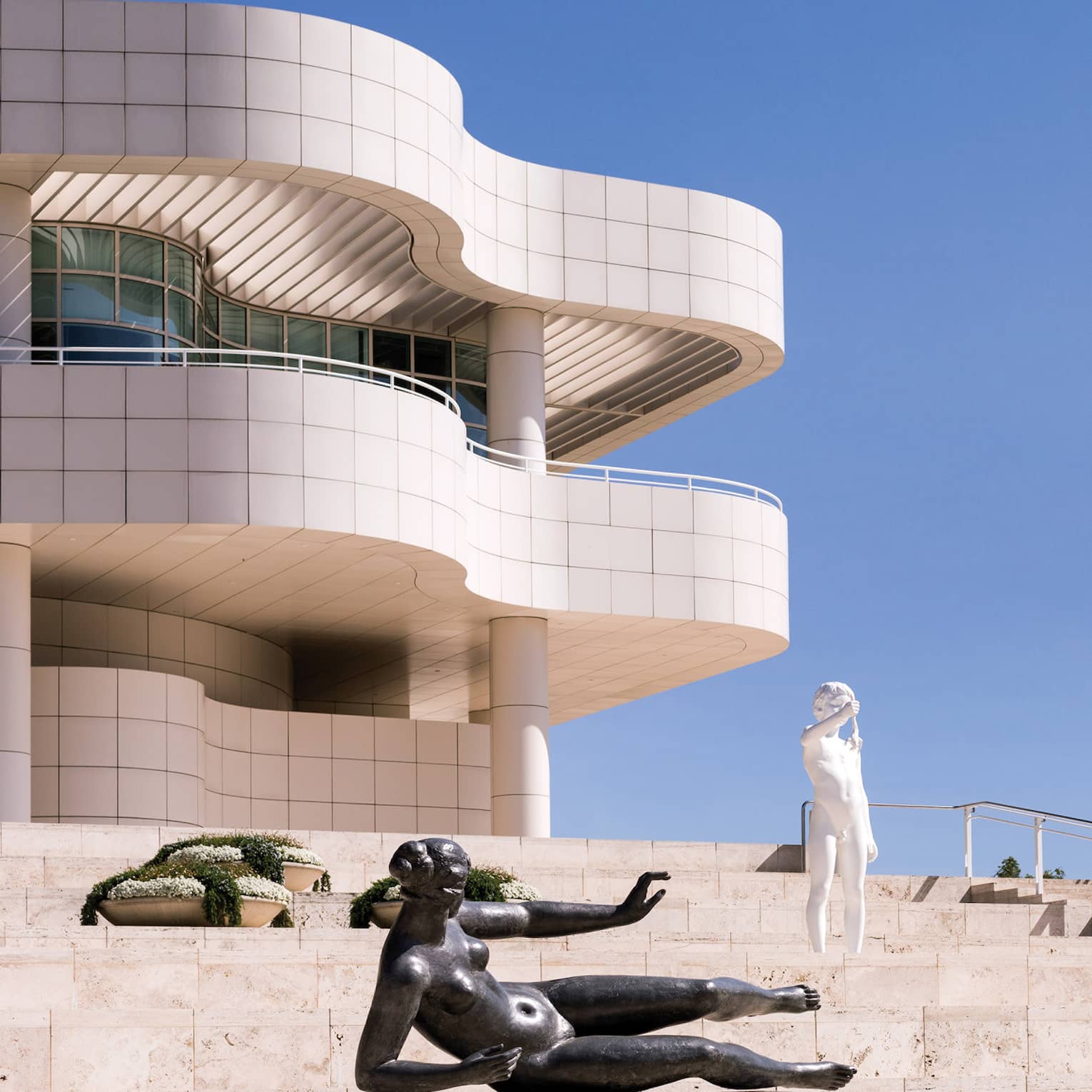 Against a cerulean sky, marble stairs dotted with statues and plants lead up to a modernist building with undulating curves.