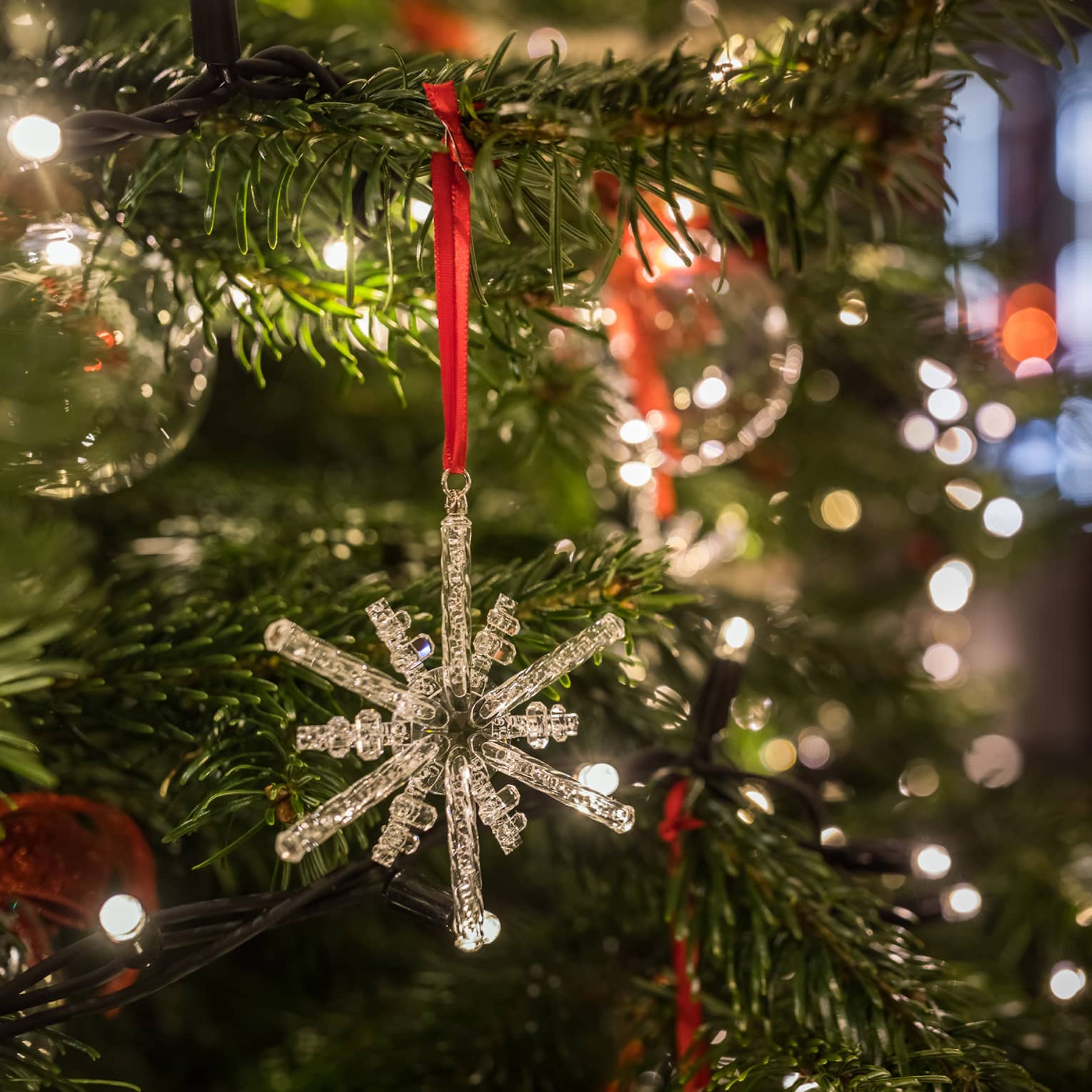 Close-up of a crystal snowflake ornament hanging on a Christmas tree with festive lights in the background
