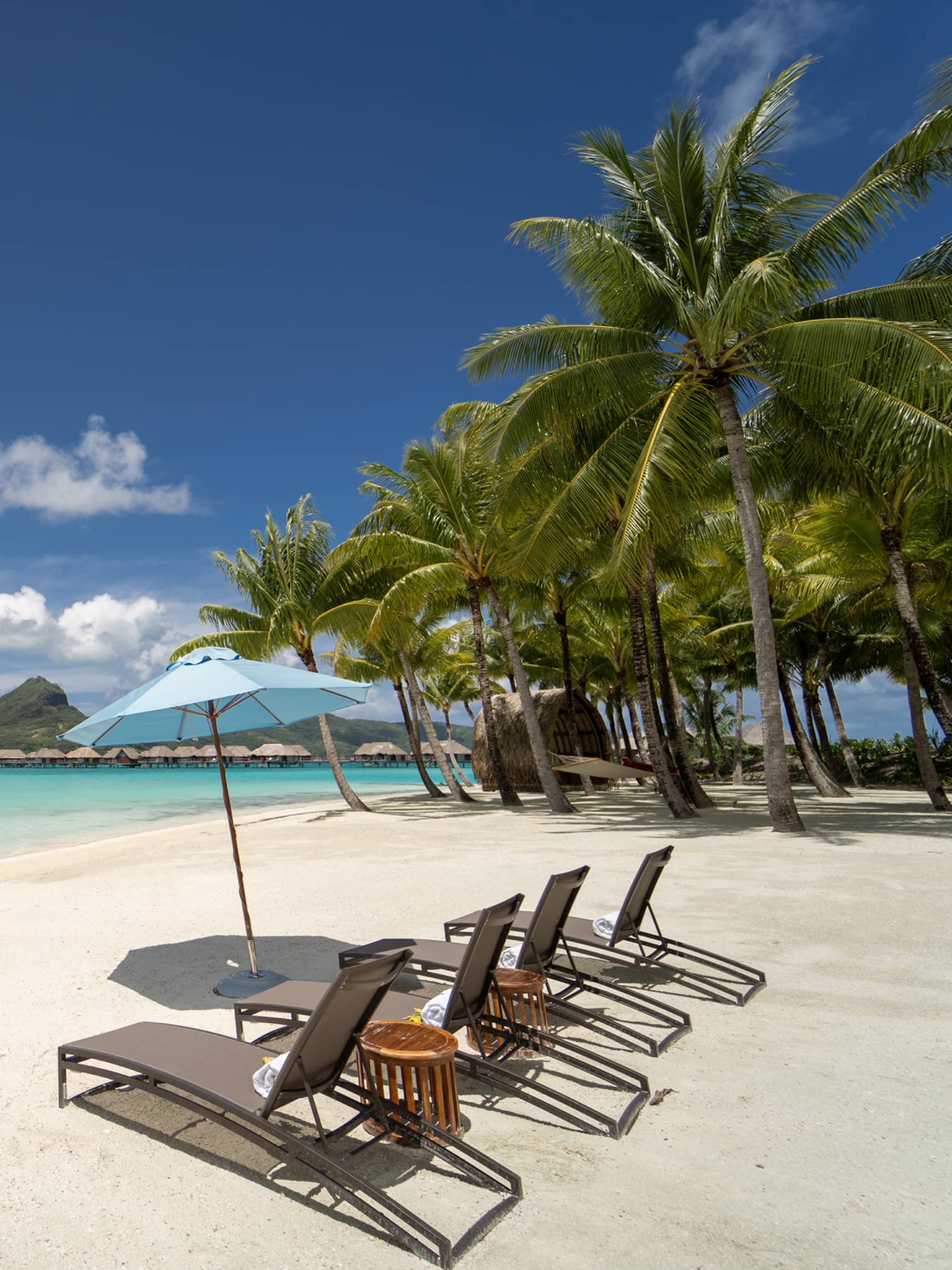 White-sand beach in Bora Bora with four lounge chairs and umbrella