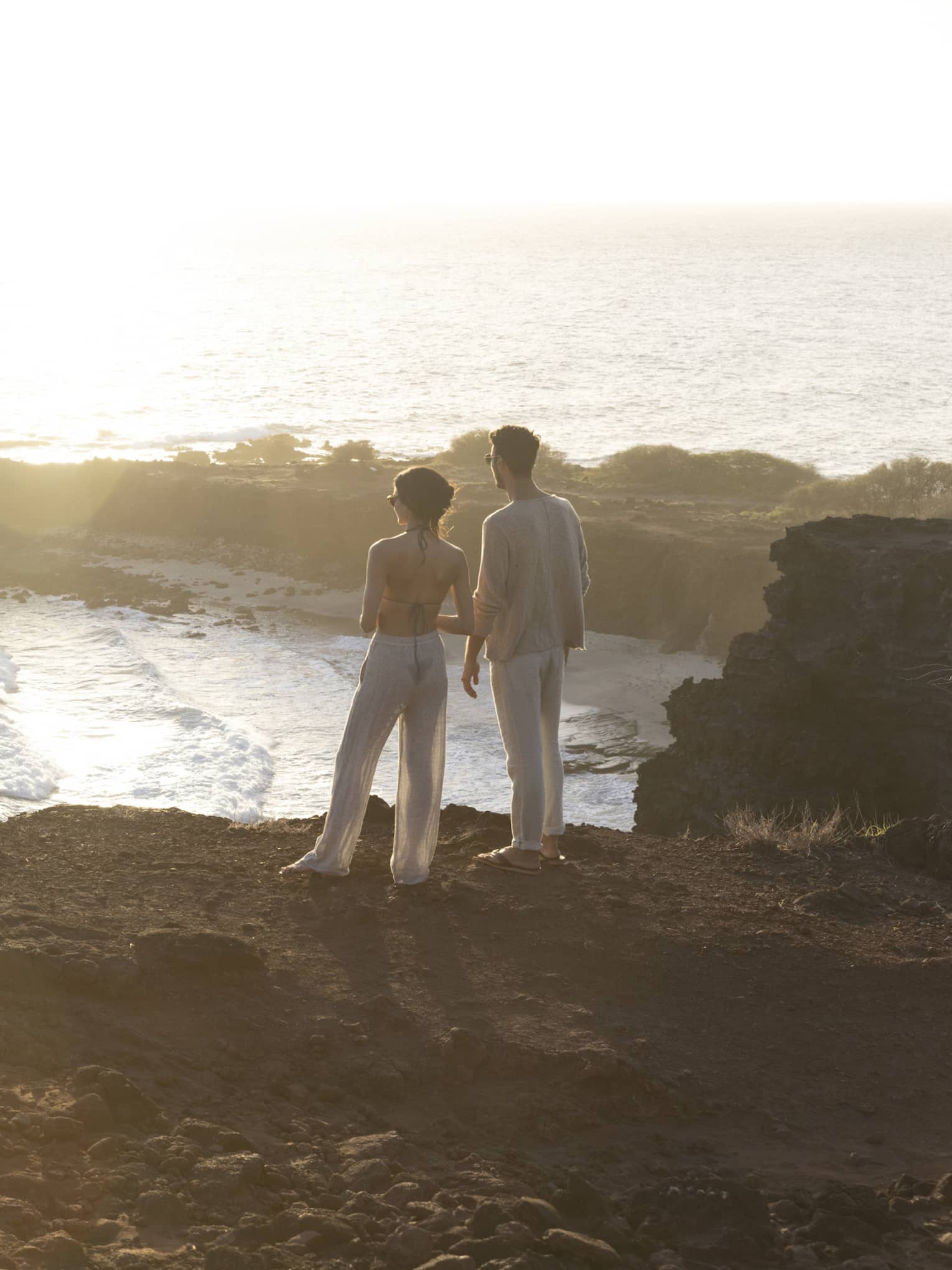 A man and woman stand on top of a cliff overlooking bay in Hawaii