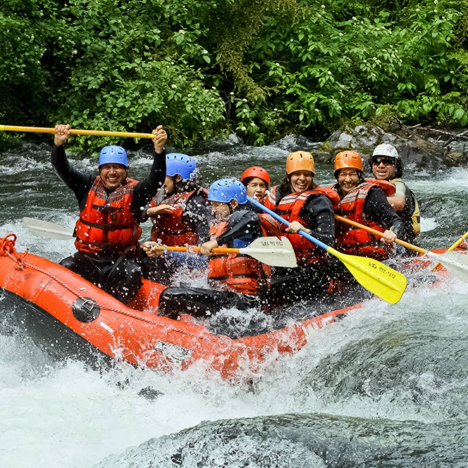 Smiling family wearing life jackets, helmets on white water raft on river rapids