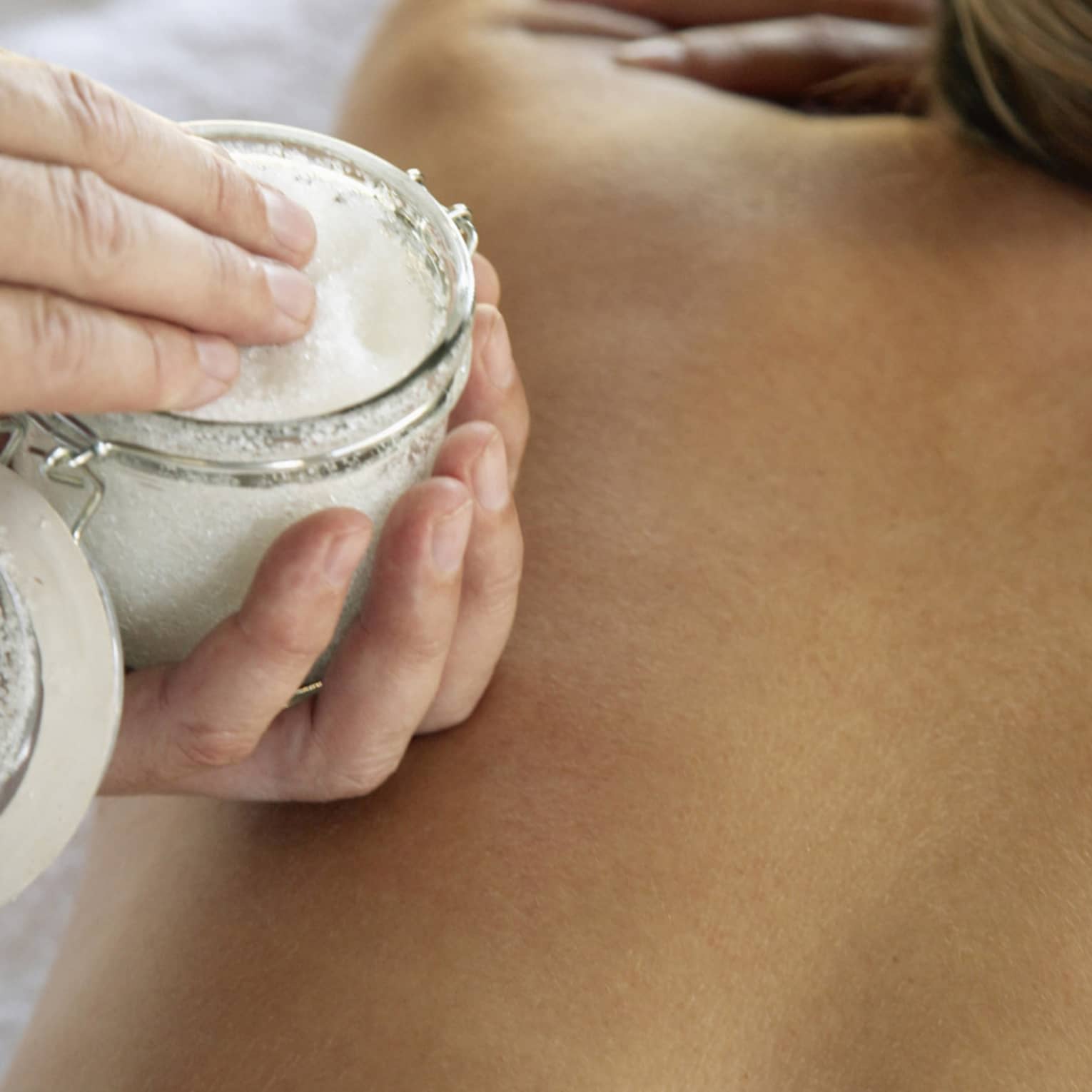 Jar of sea salt scrub above woman's bare back in spa