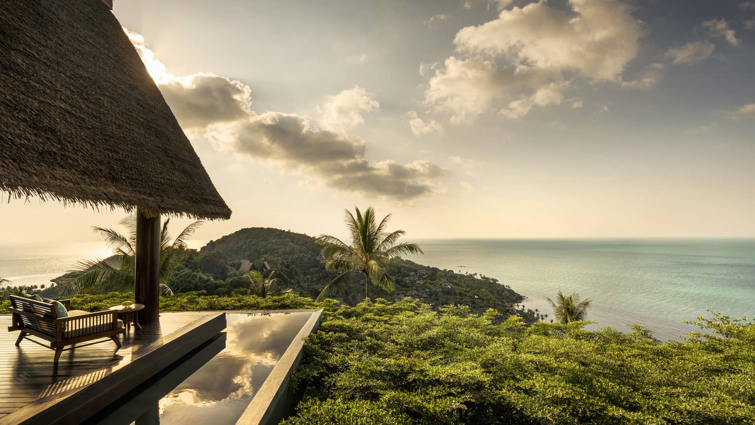 Patio lounge chair, thatched roof and deck overlooking canopy of tropical trees, ocean