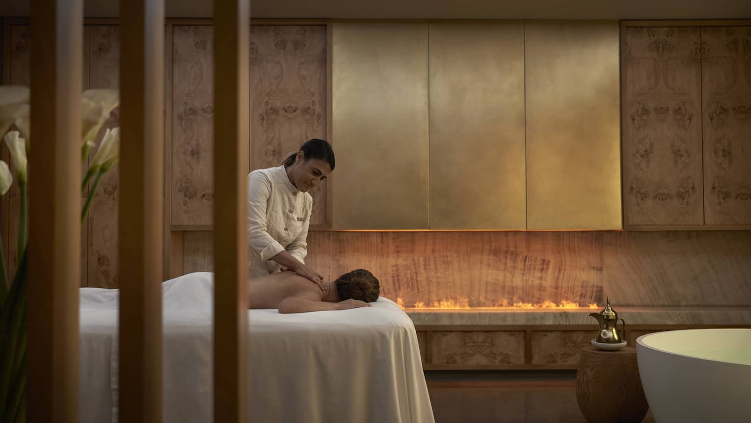 Person facedown on white spa table receiving massage from spa therapist