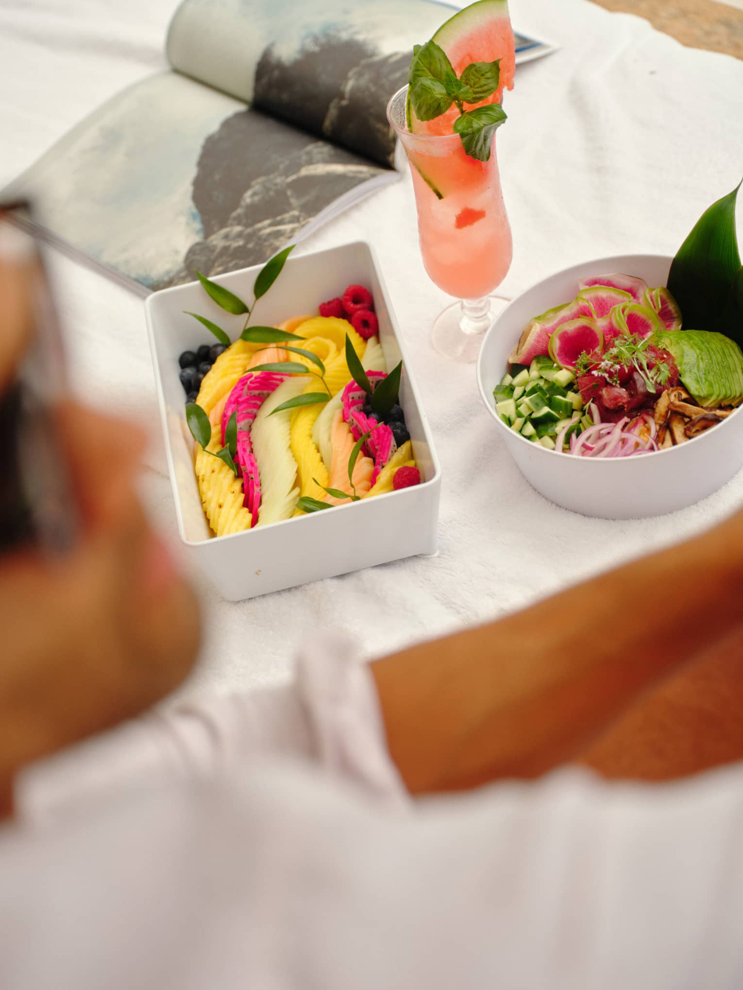 Fresh fruit and salad in white containers set on a day bed