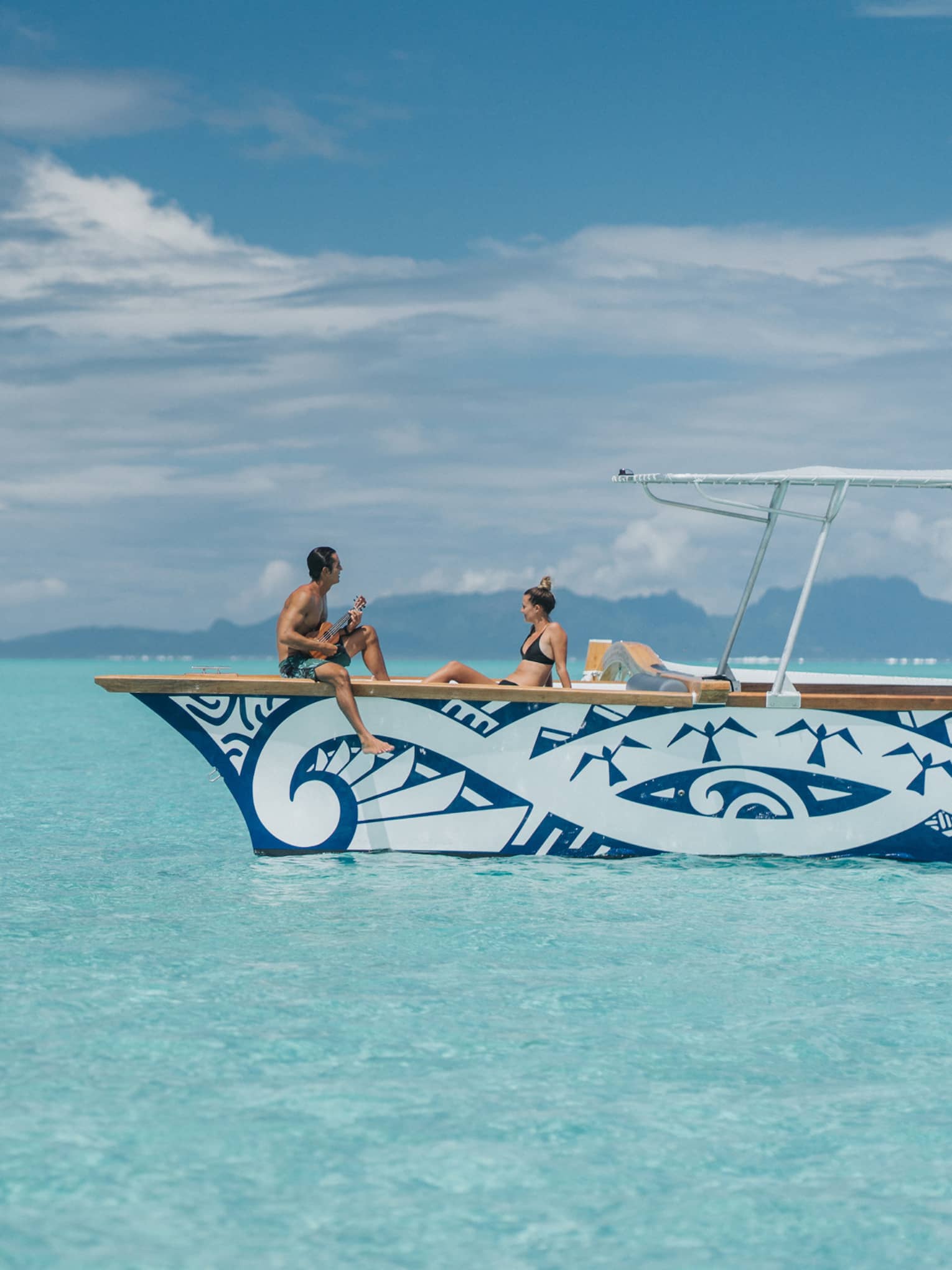 Man plays ukulele for woman on catamaran boat on lagoon