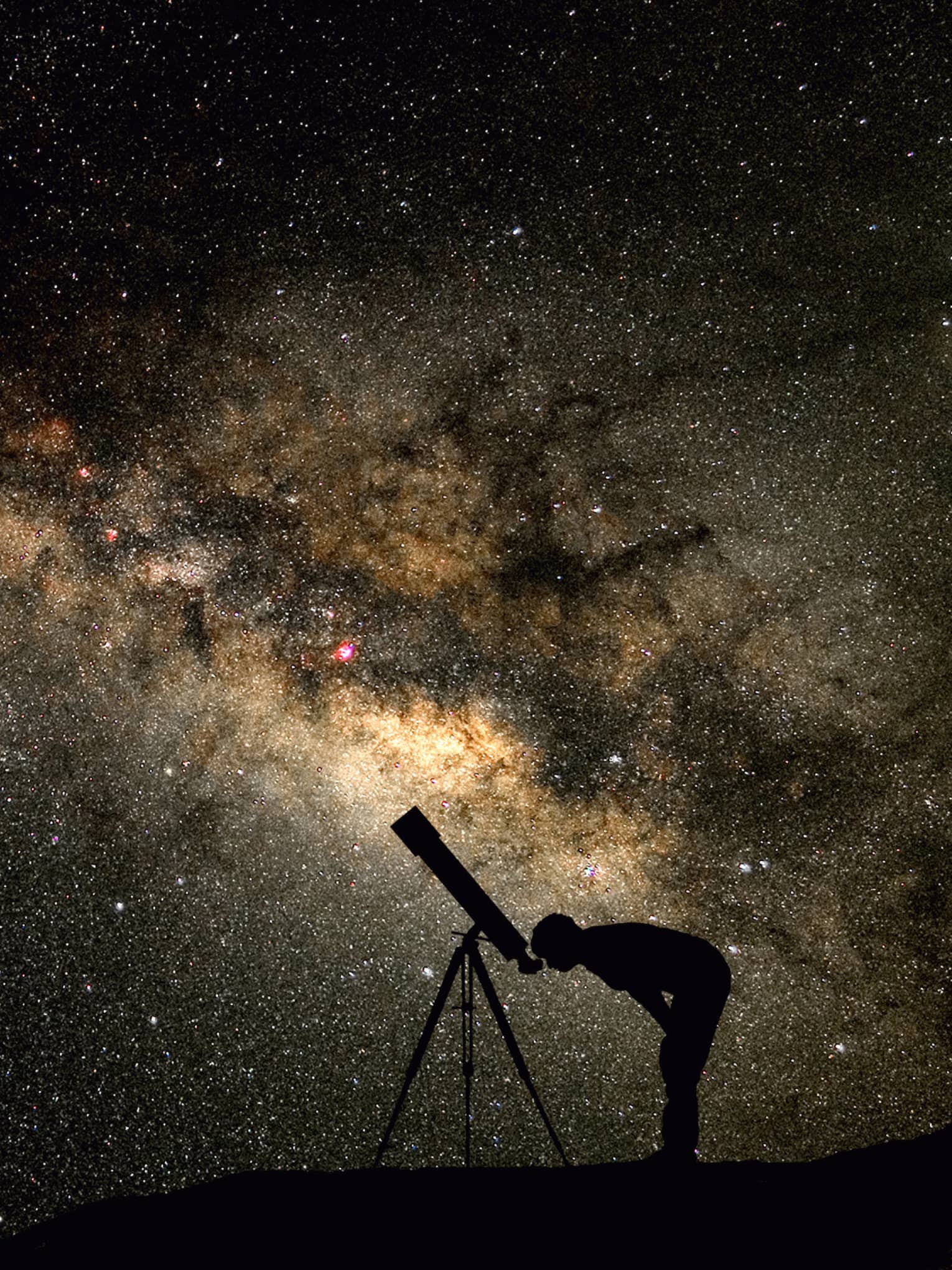 Silhouette of stargazer leaning into telescope against a starry sky, milky way