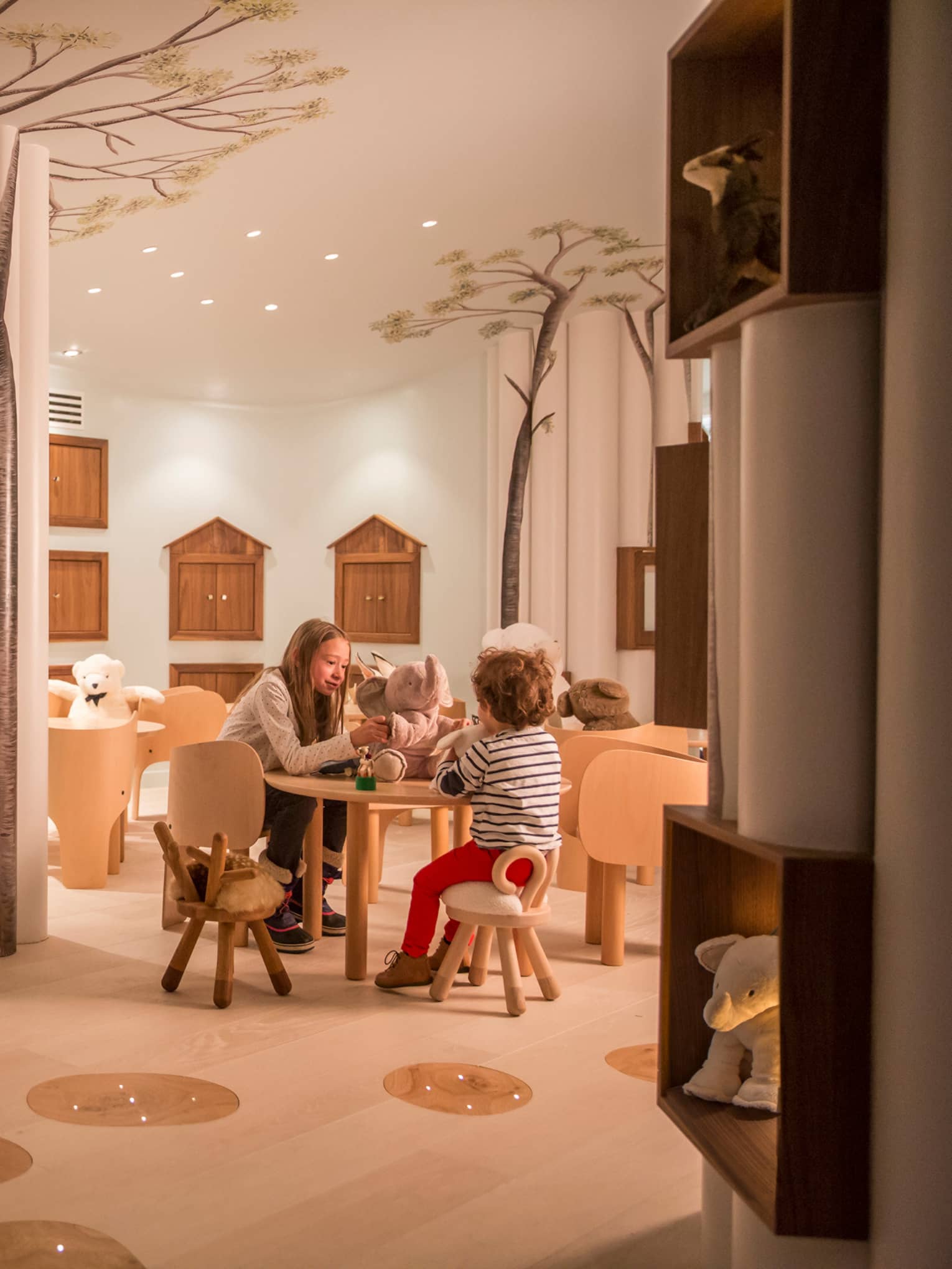 Kids play with toys at small table near chairs, stuffed bears in Kid Kingdom playroom