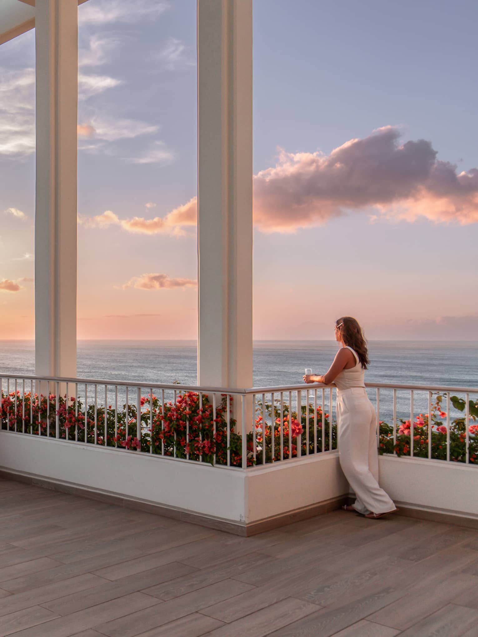 Woman gazes out to sunset view over the ocean from expansive terrace