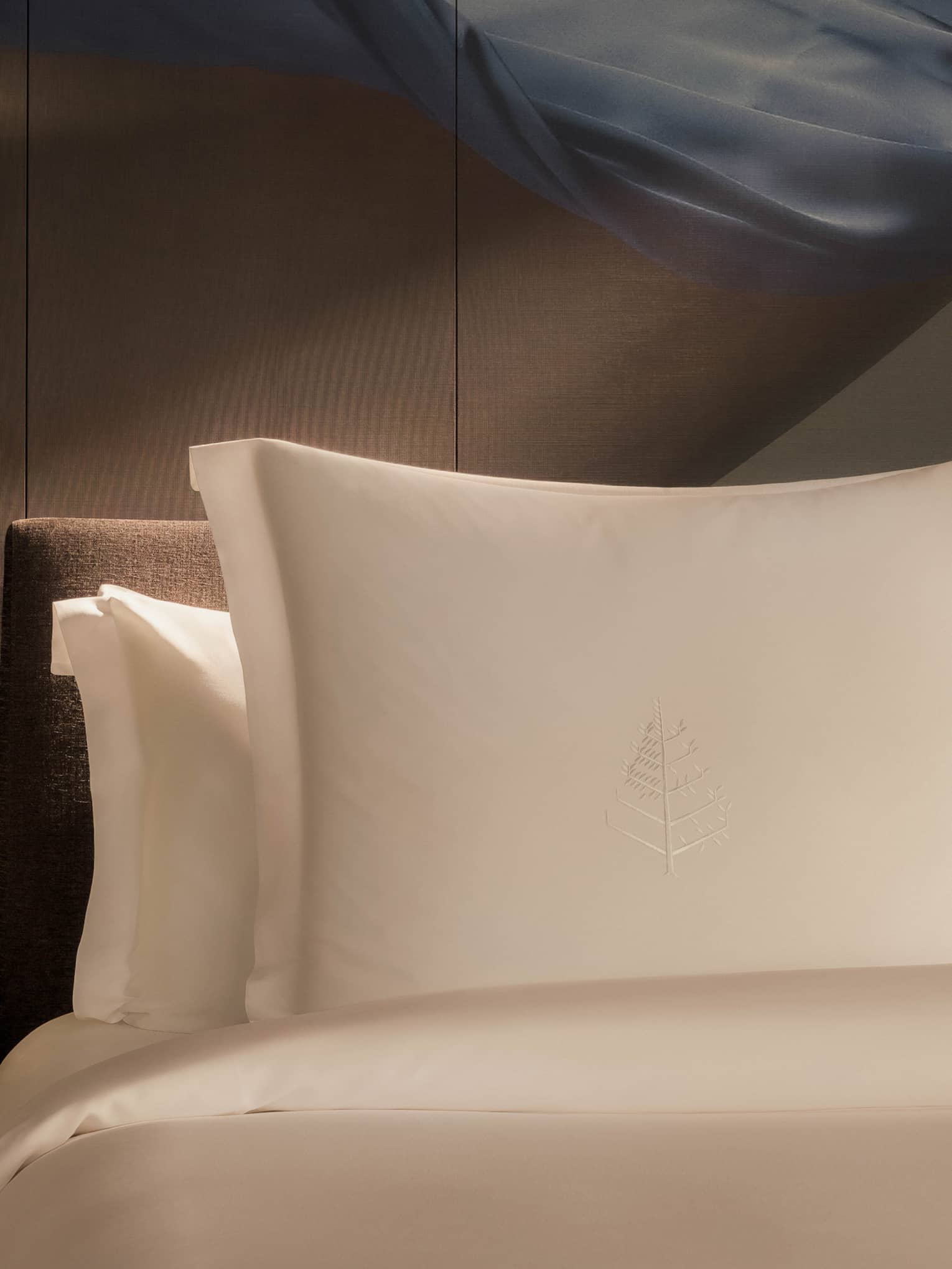 Luxury hotel room bed with artistic accent wall behind white pillows and sheets, and a wooden side table with flowers