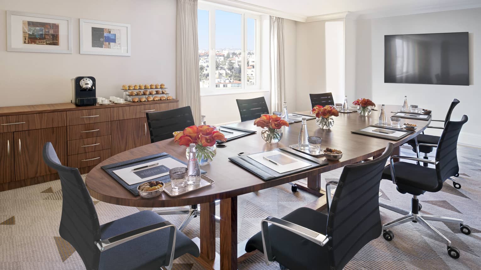 A circular mahogany table in the centre of an eggshell coloured boardroom surrounded by office chairs. 