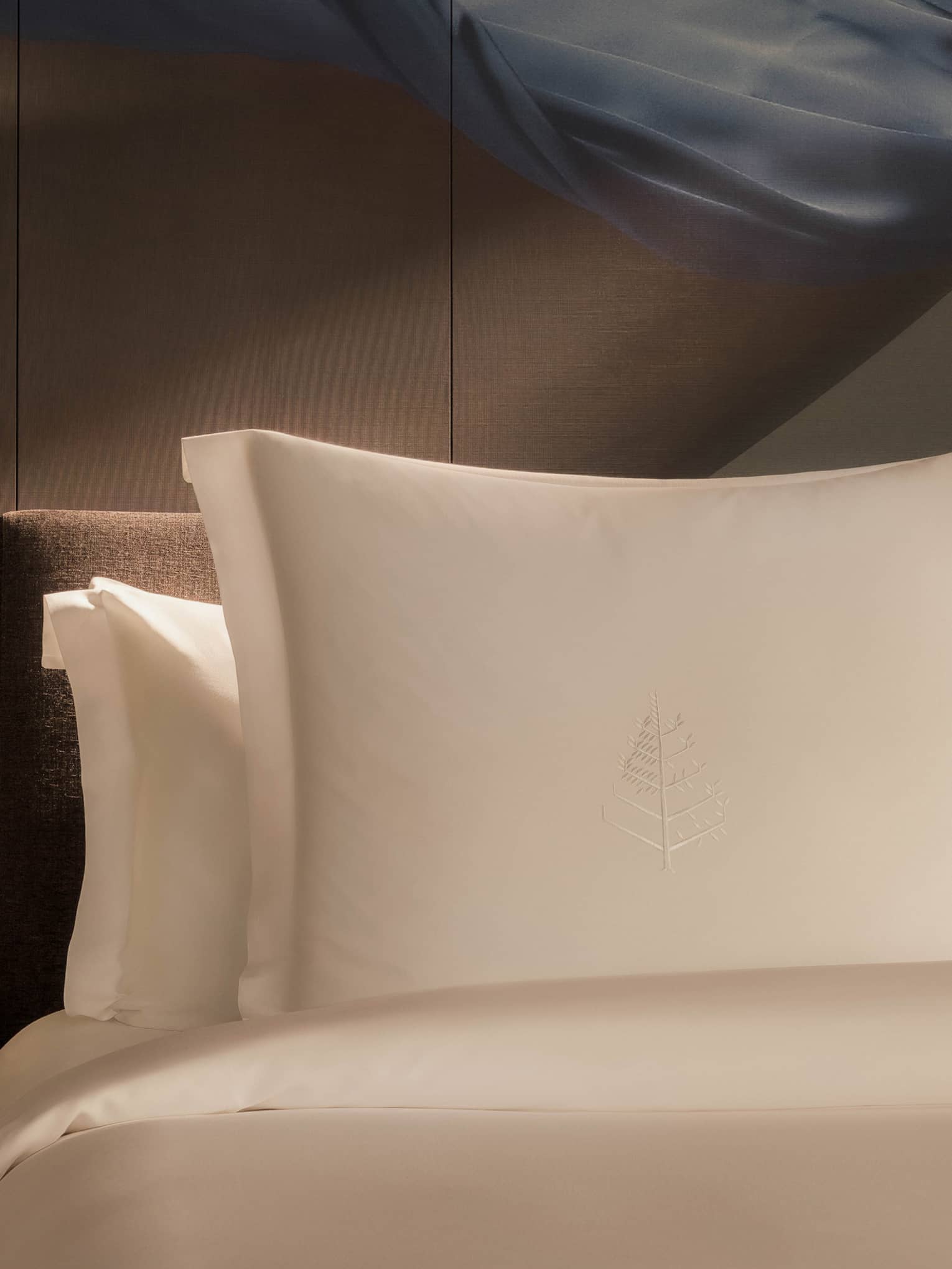 Luxury hotel room bed with artistic accent wall behind white pillows and sheets, and a wooden side table with flowers