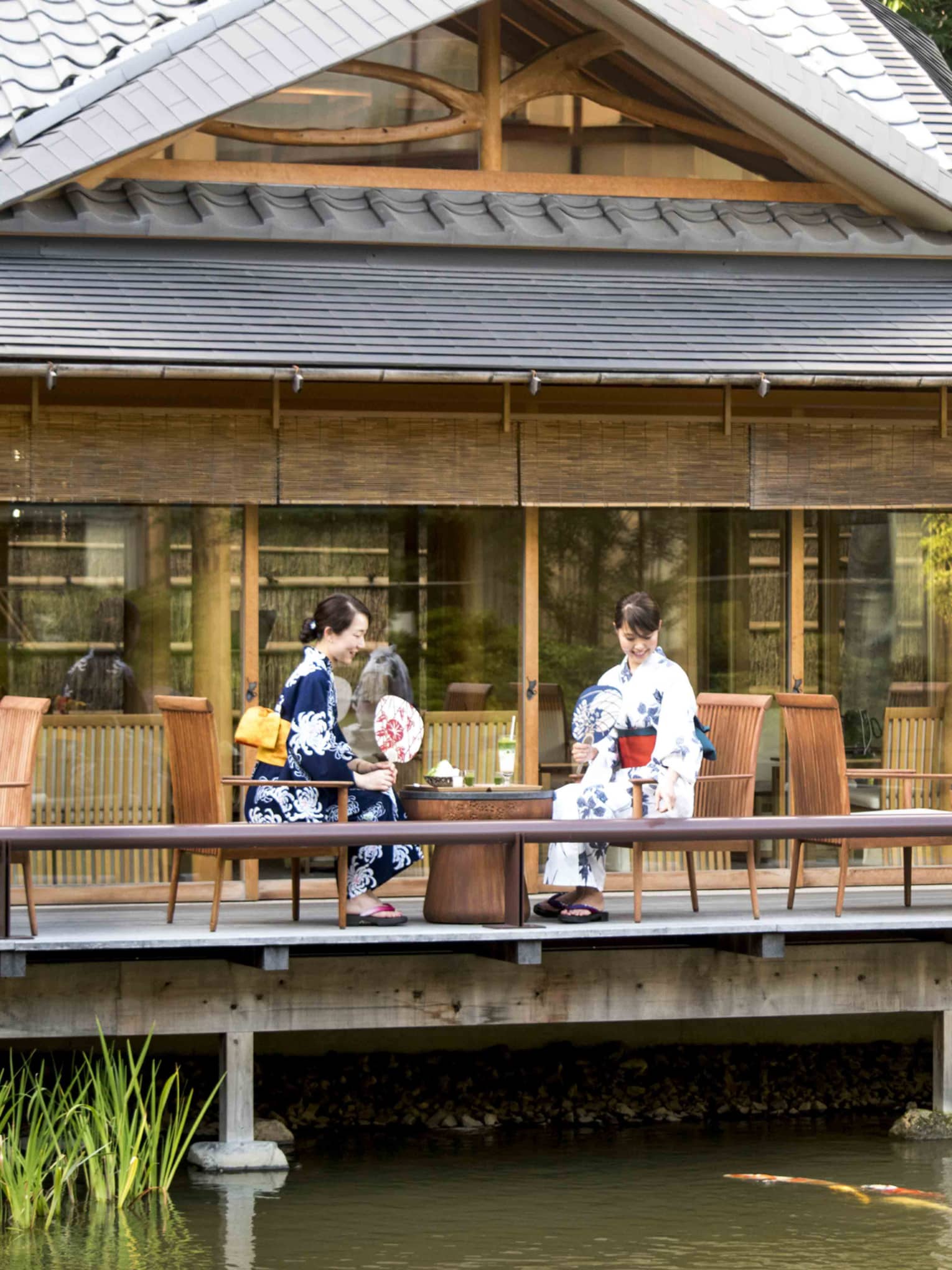 Two women in traditional Japanese garb observing the koi fish swimming below