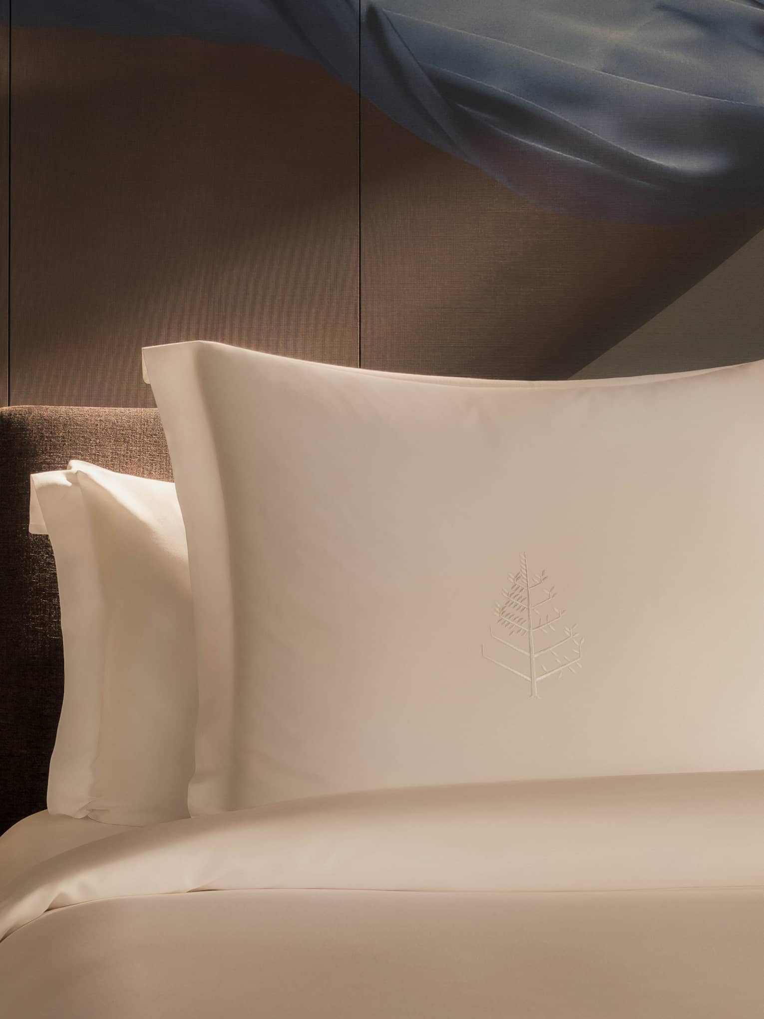 Luxury hotel room bed with artistic accent wall behind white pillows and sheets, and a wooden side table with flowers