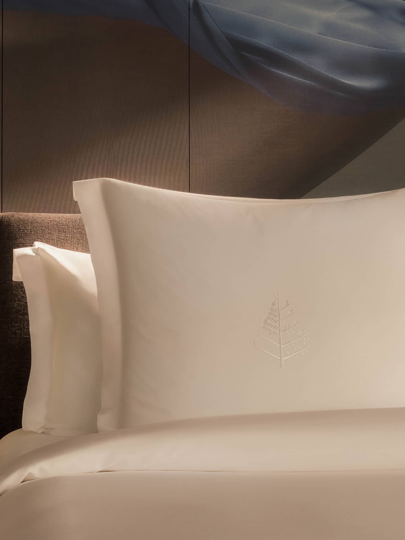 Luxury hotel room bed with artistic accent wall behind white pillows and sheets, and a wooden side table with flowers