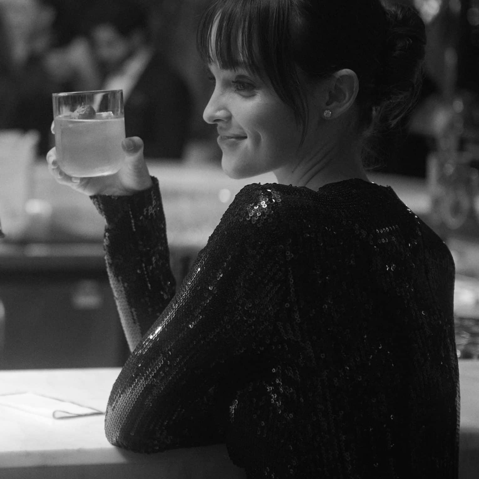 A black and white shot of two elegantly dressed guests at a bar, smiling and raising their cocktails.