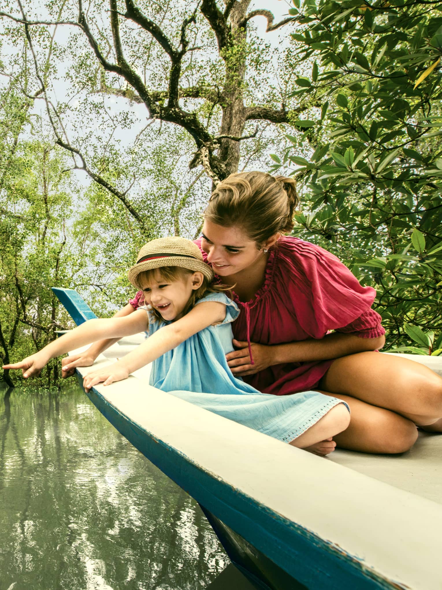 Mom, young daughter in back of wood canoe look into river