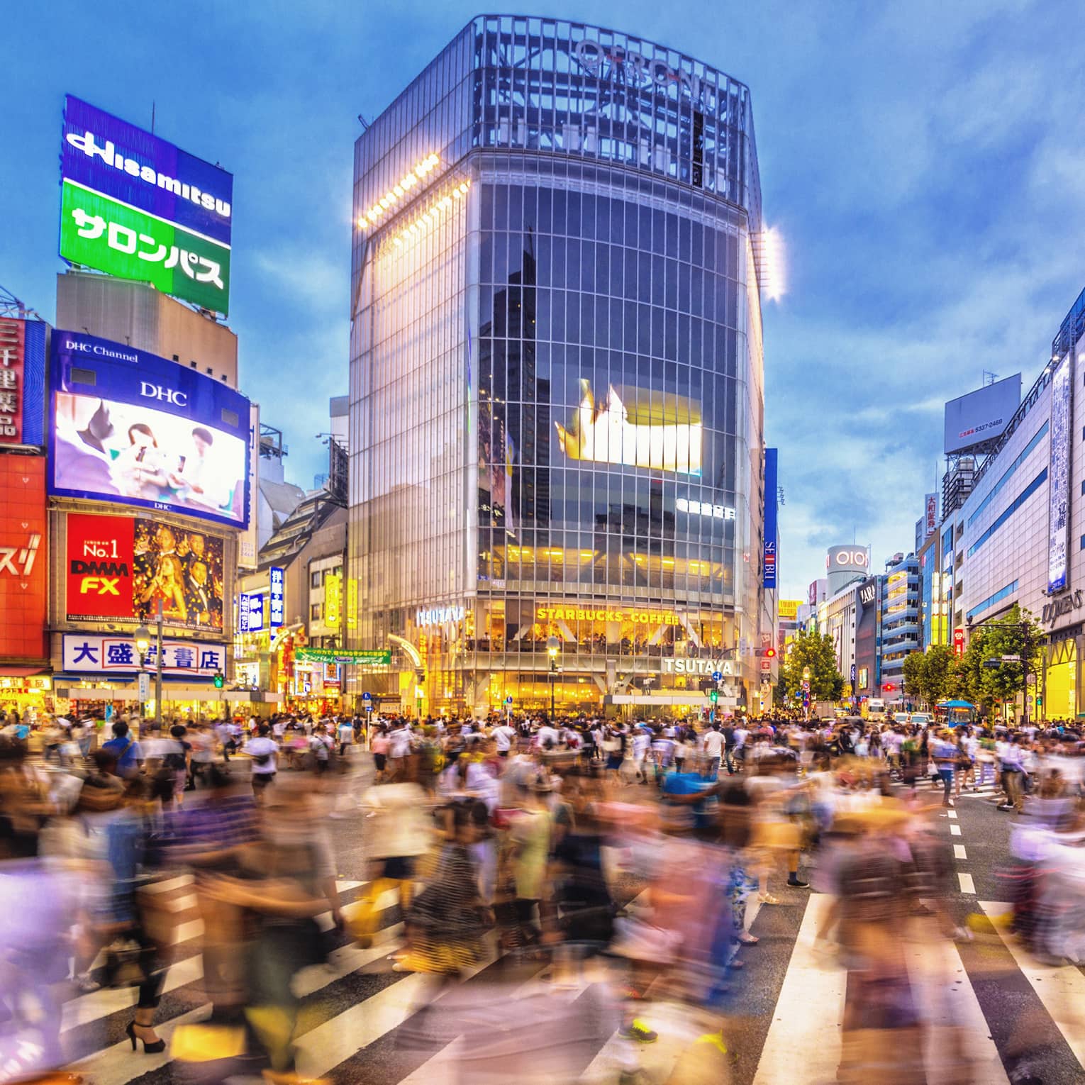 Image of blurry crowds along sidewalk under glass buildings, colourful billboards at night