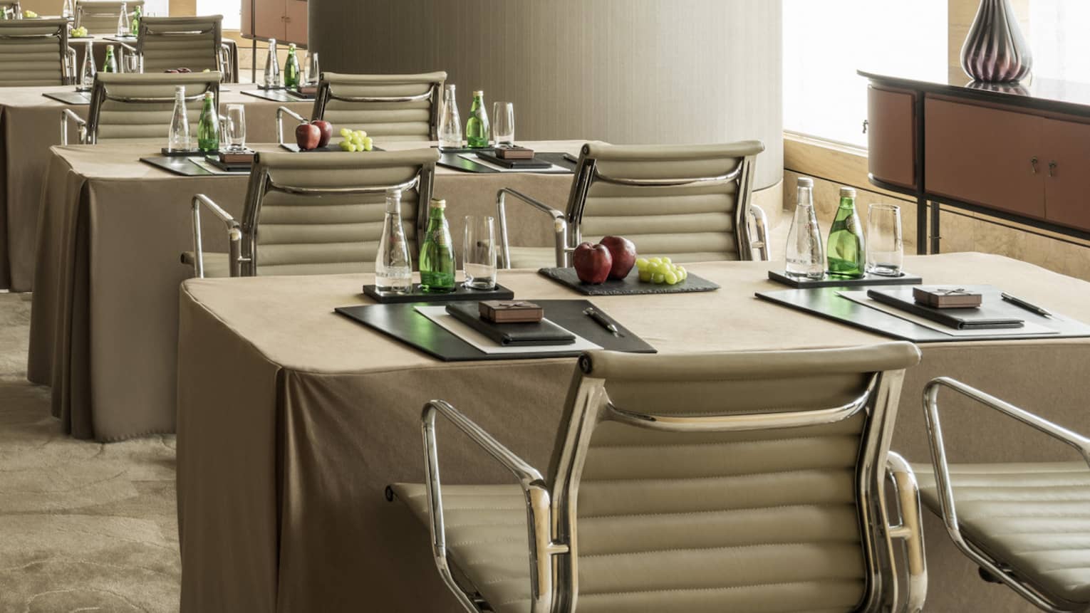 Conference room with rows of small tables, pairs of chairs facing screen, large pillar 