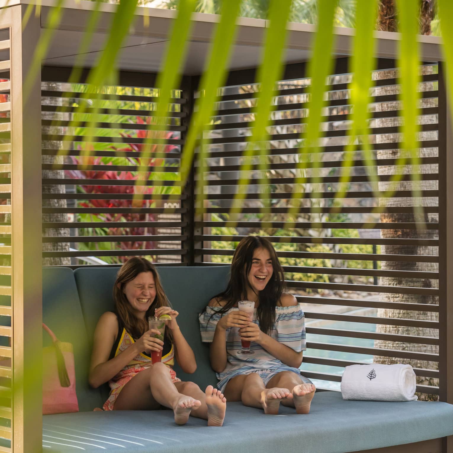 Two women resting near an outdoor pool with drinks.