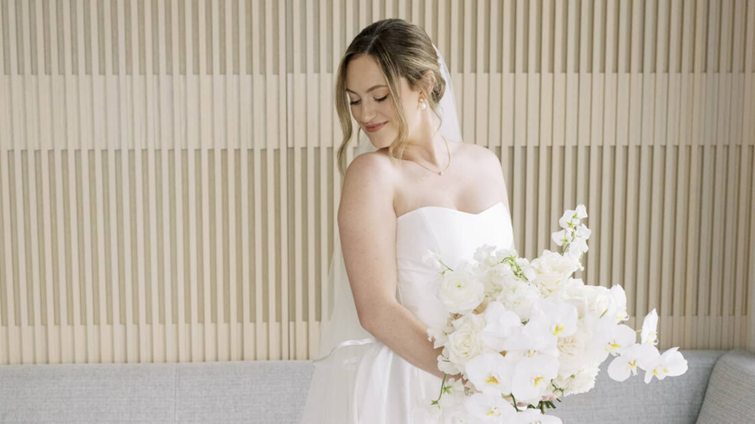 A bride poses in a wedding dress and veil holding a large white bouquet