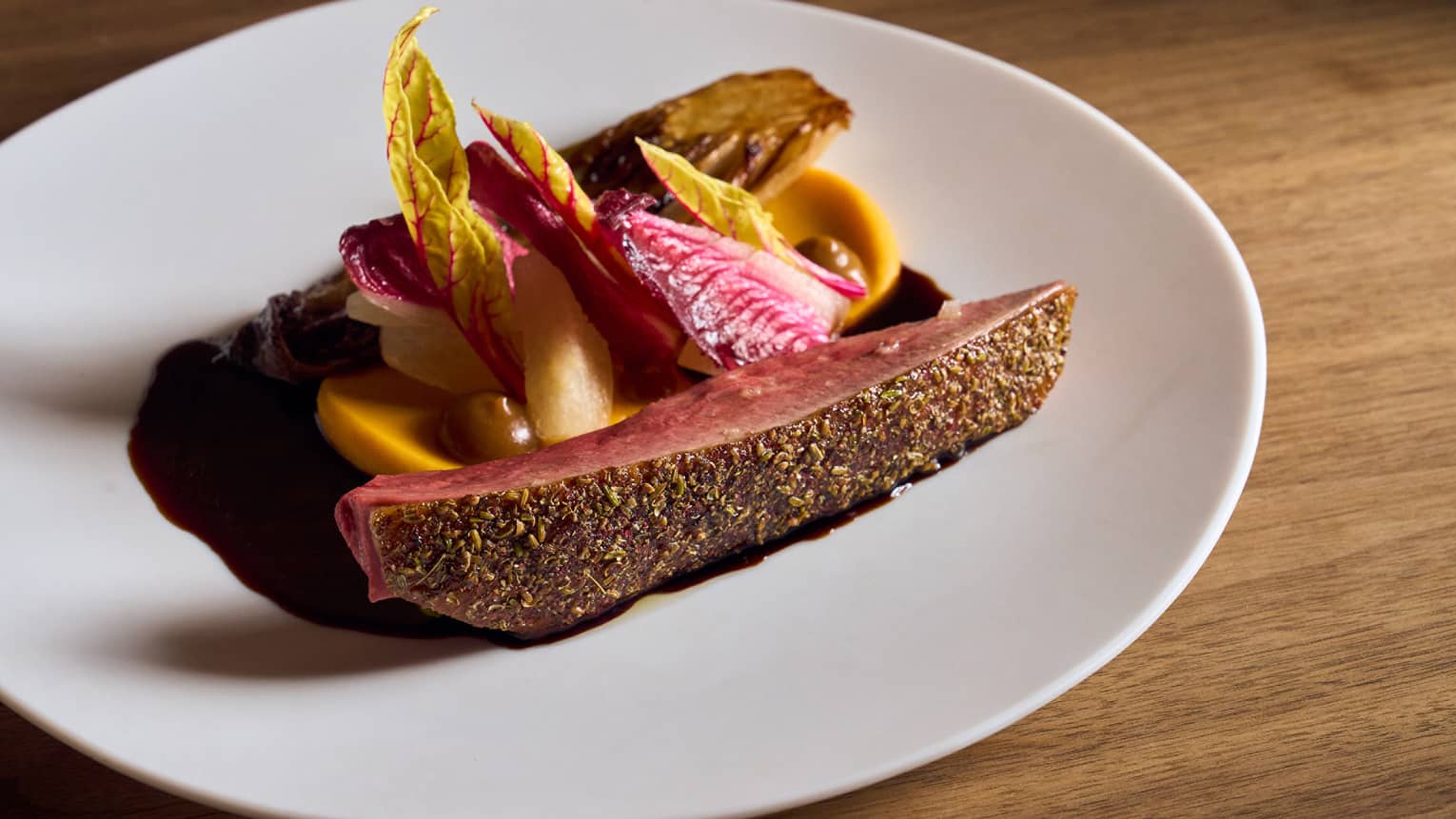A round white plate holds slices of meat with colourful garnishes and a sauce.