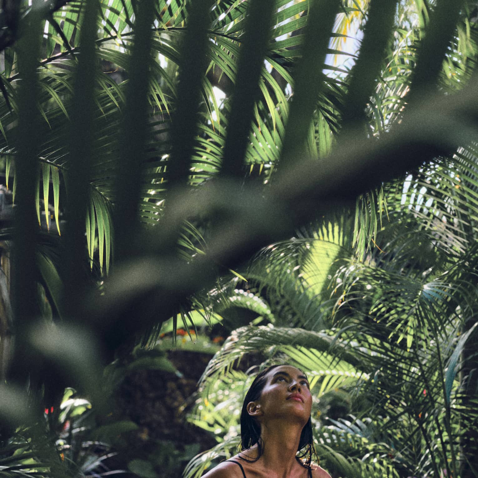 A woman in a black bathing suit walks through lush rainforest
