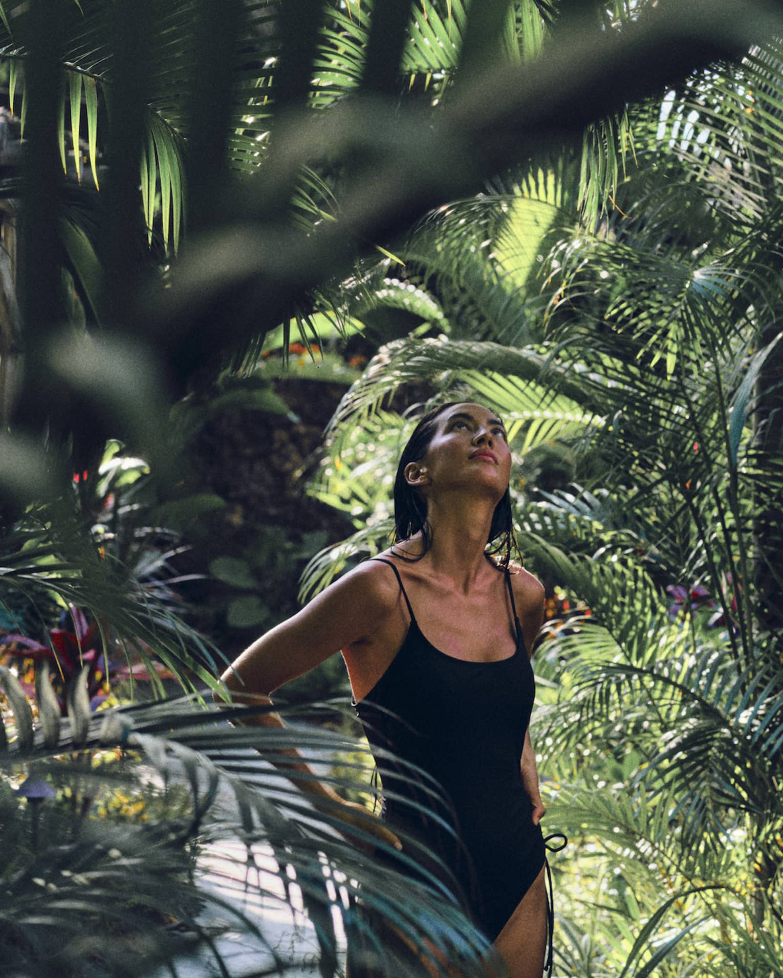 A woman in a black bathing suit walks through lush rainforest