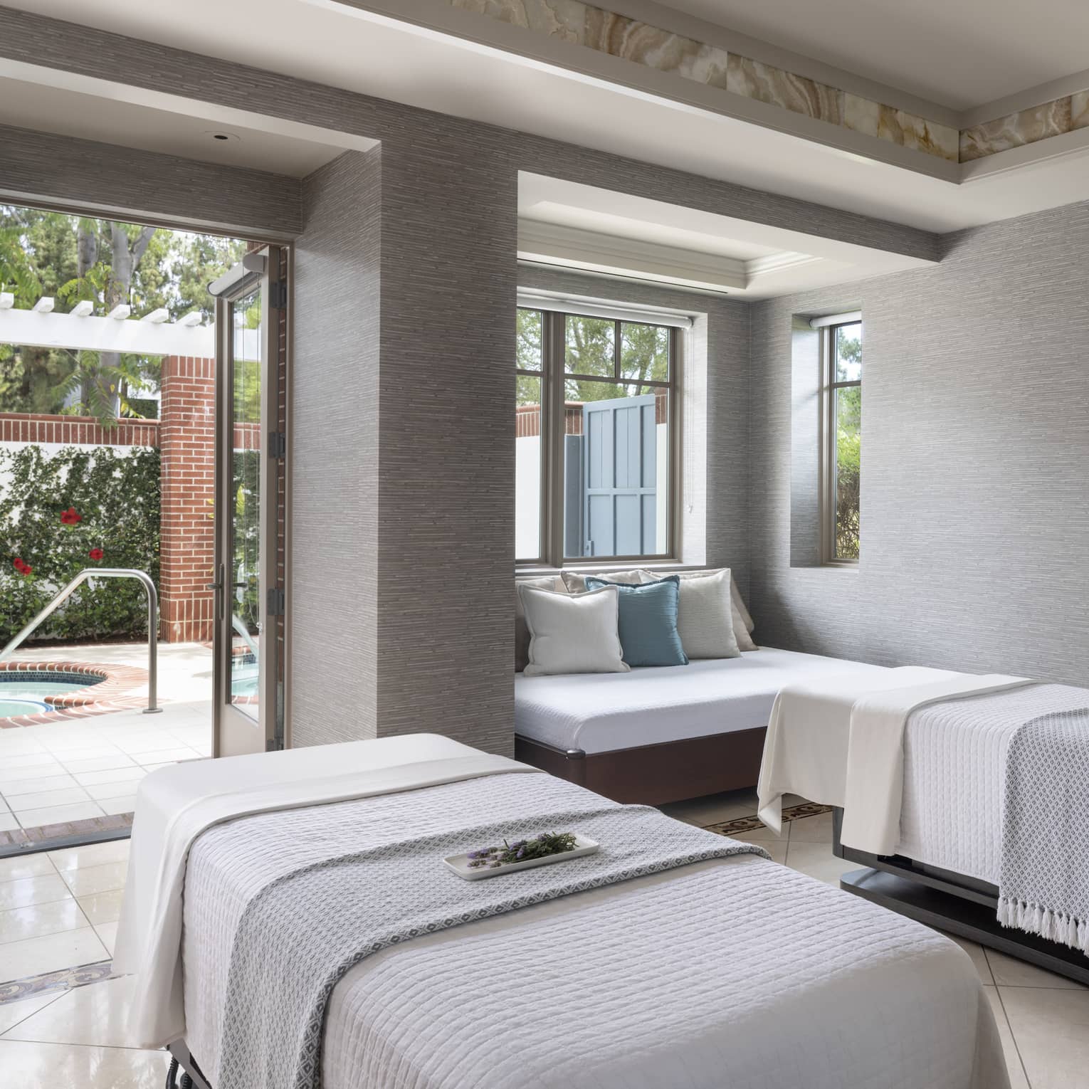 A spa treatment room with two massage beds, a small couch and an open door leading outside.