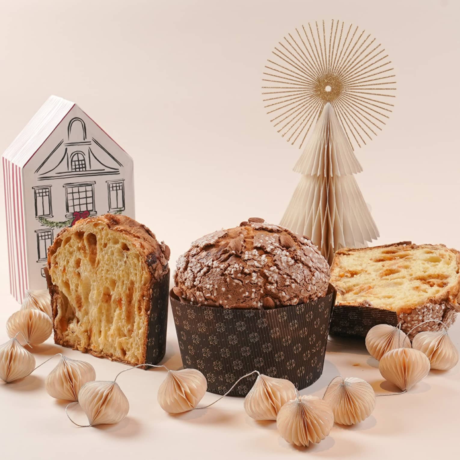 One whole panetonne and one sliced in half set on a white backdrop next to paper holiday decorations