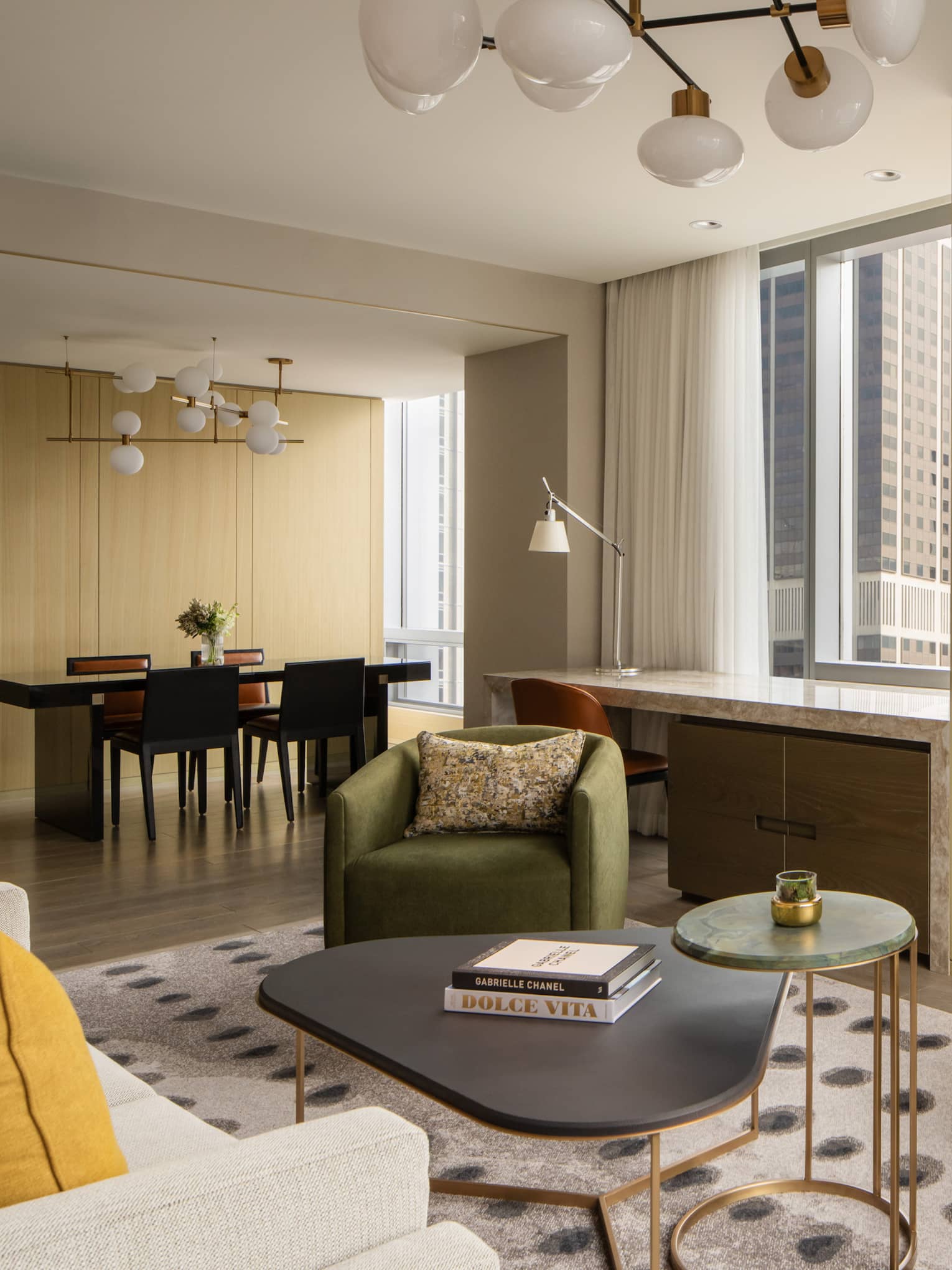 Luxury suite living area with a dining table and four chairs, desk, green armchairs, beige sofa, bar cabinet with glassware, TV and large windows