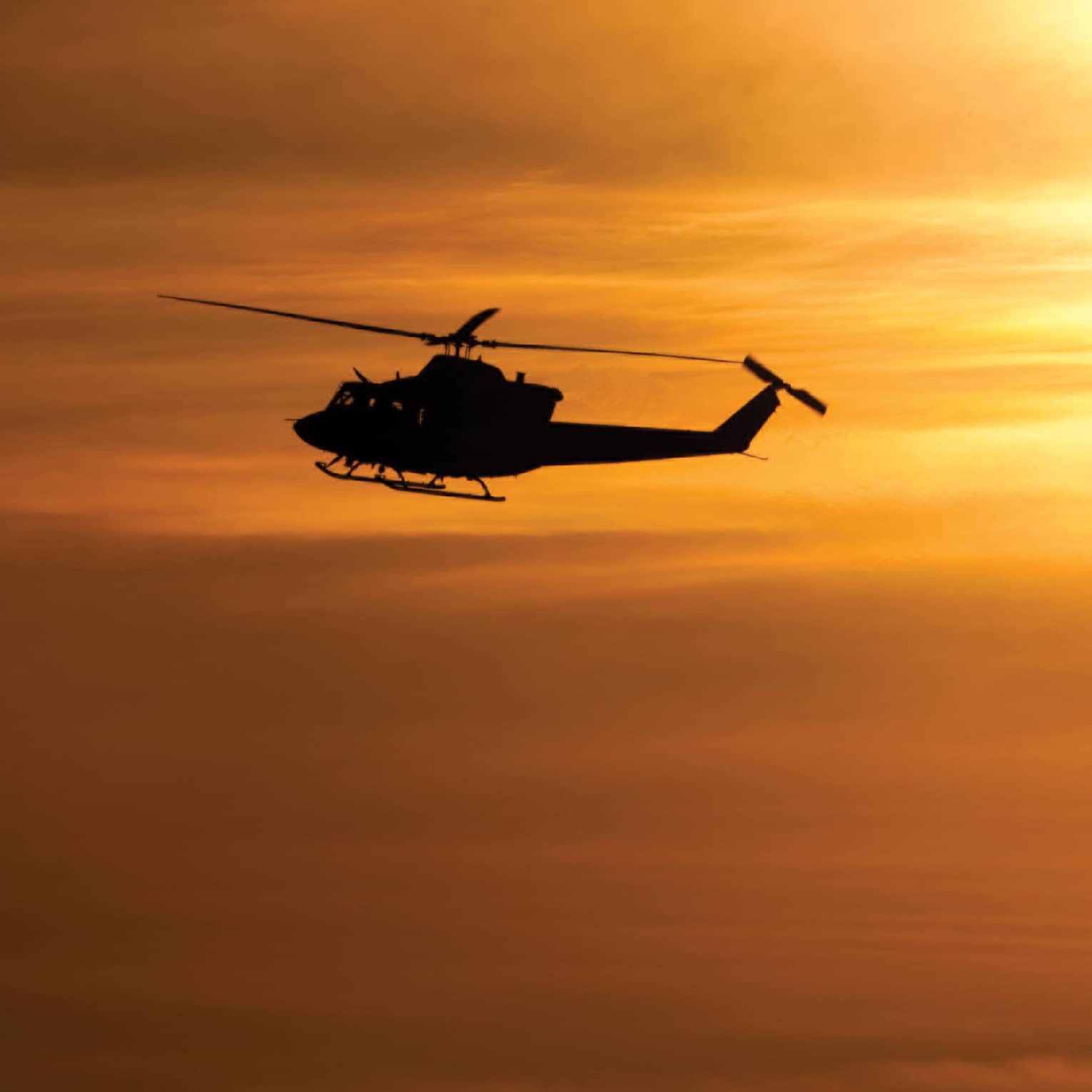 Silhouette of helicopter against orange sky