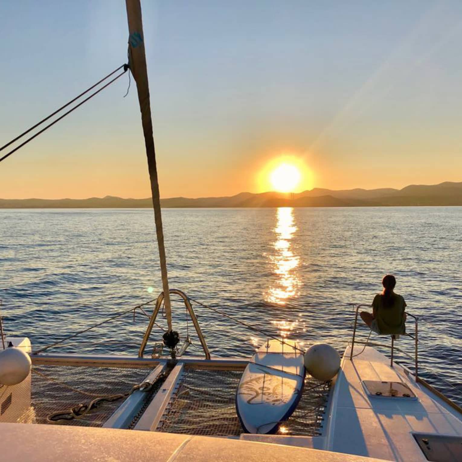 Two guests lounge on luxury sailboat near stern railing at sunset