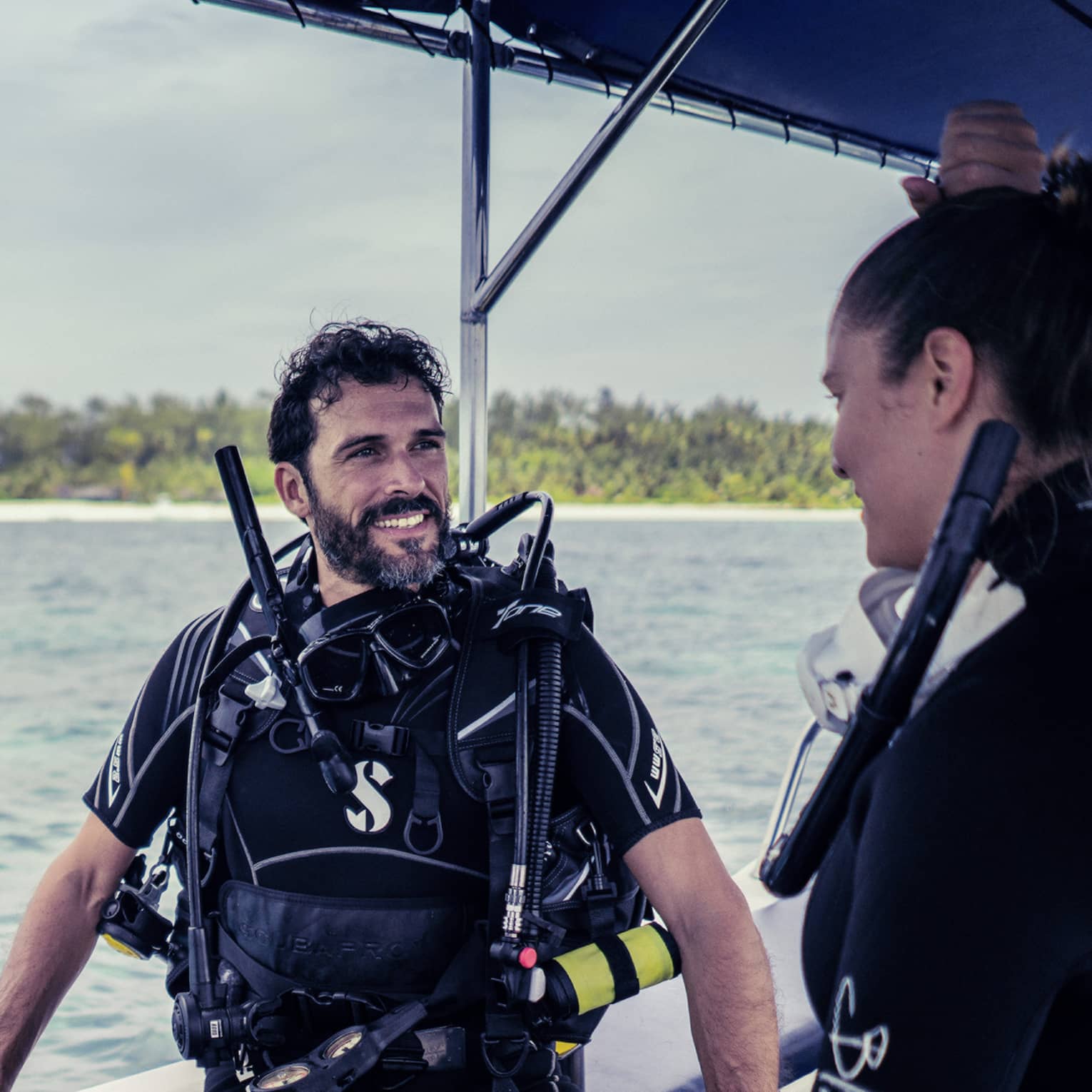 Three people in SCUBA gear with tanks on boat in ocean smiling and talking 