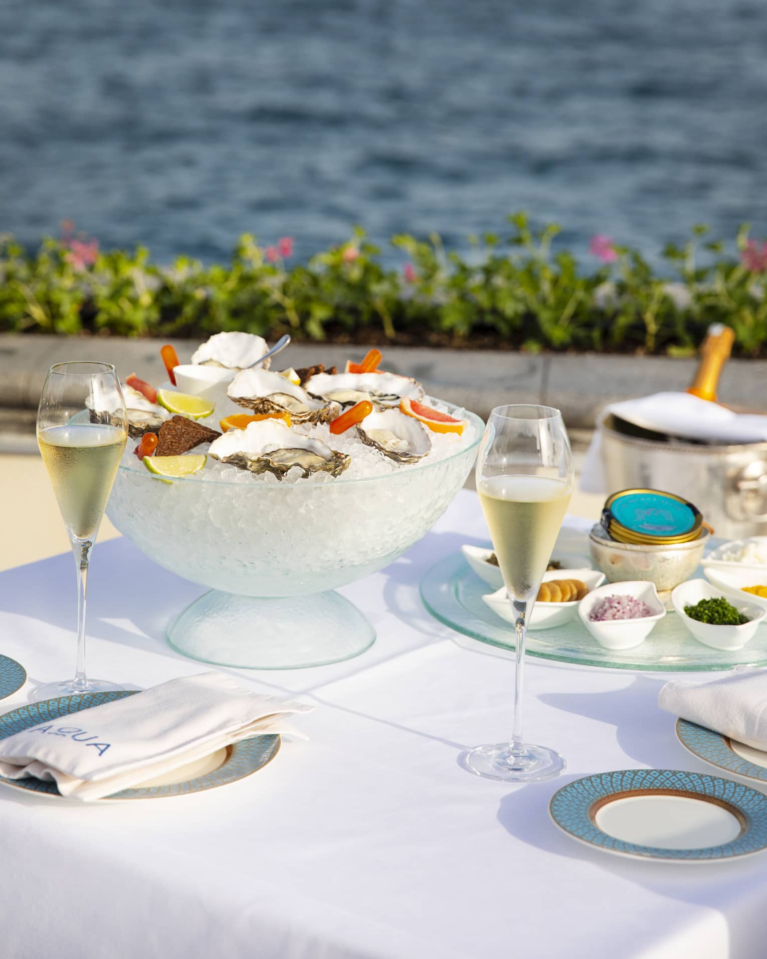 Square table with white linens, blue dinnerware, a bowl of ice with oysters on the half shell, Sea of Marmara in the background