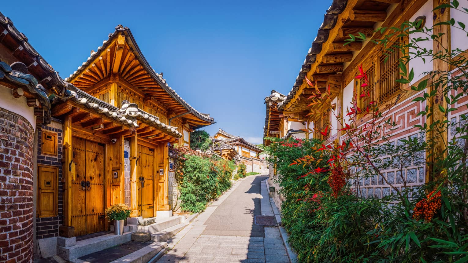 Stone walkway framed by wooden architecture and foliage with red flowers