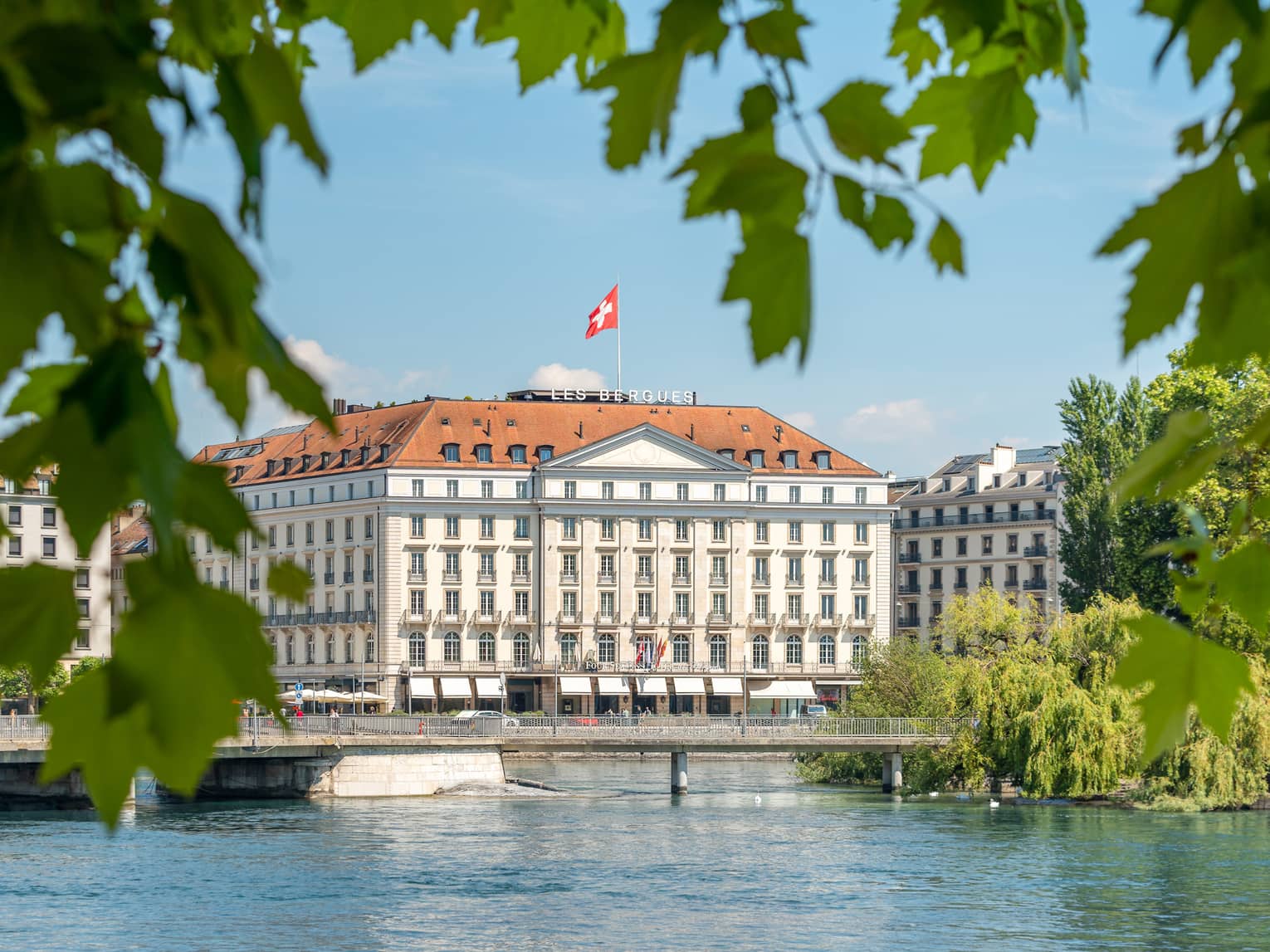 Four Seasons Hotel Geneva surrounded by green foliage, Lake Geneva in the foreground