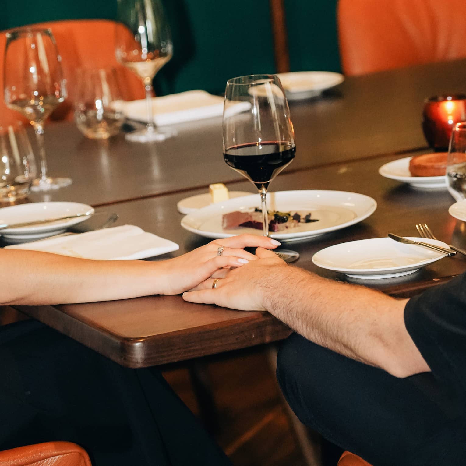 Two people hold their hands together on top of a restaurant dining table