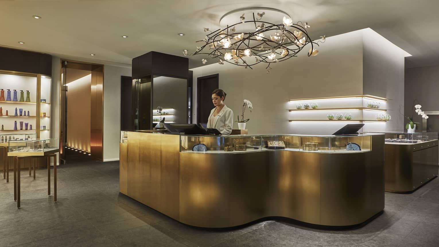 A golden reception desk rests under a black chandelier in the lobby of the Four Seasons Toronto. 