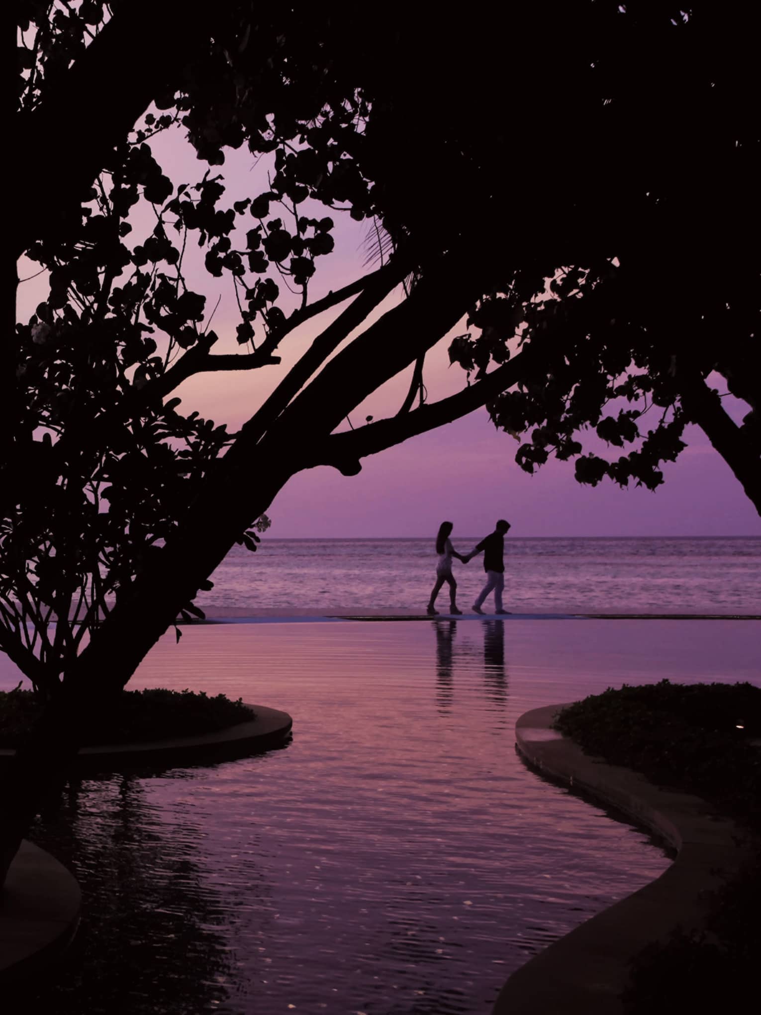 Serenity Pool winding around trees at sunset, silhouette of couple in background