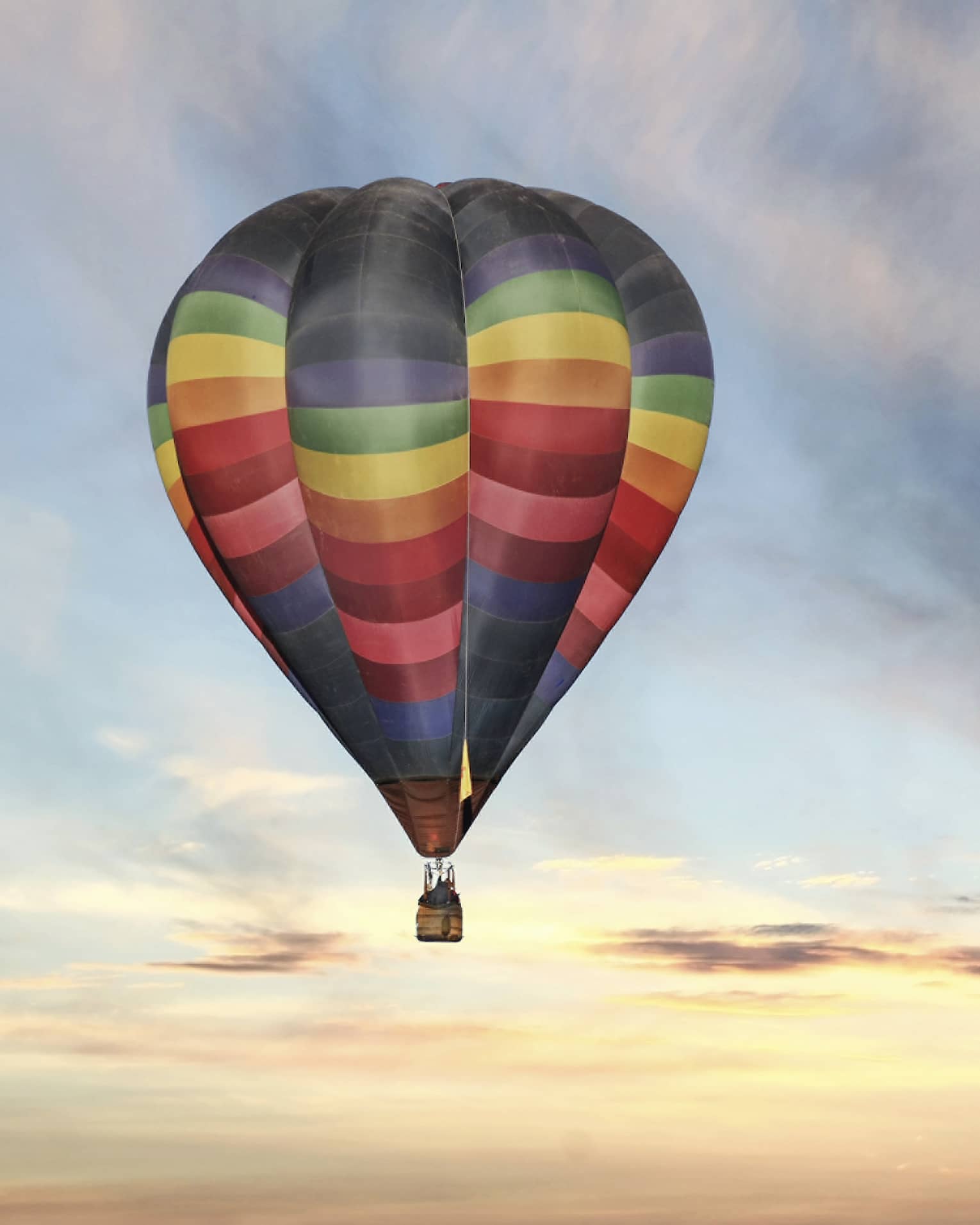 Rainbow-striped hot air balloon floats in the sky at sunset