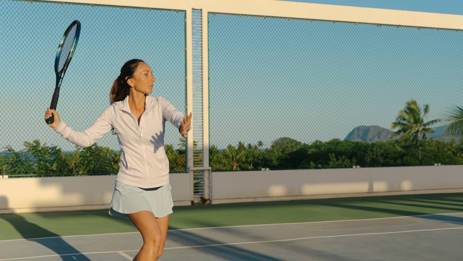 A woman gets ready to hit a tennis ball on a court in tropical destination