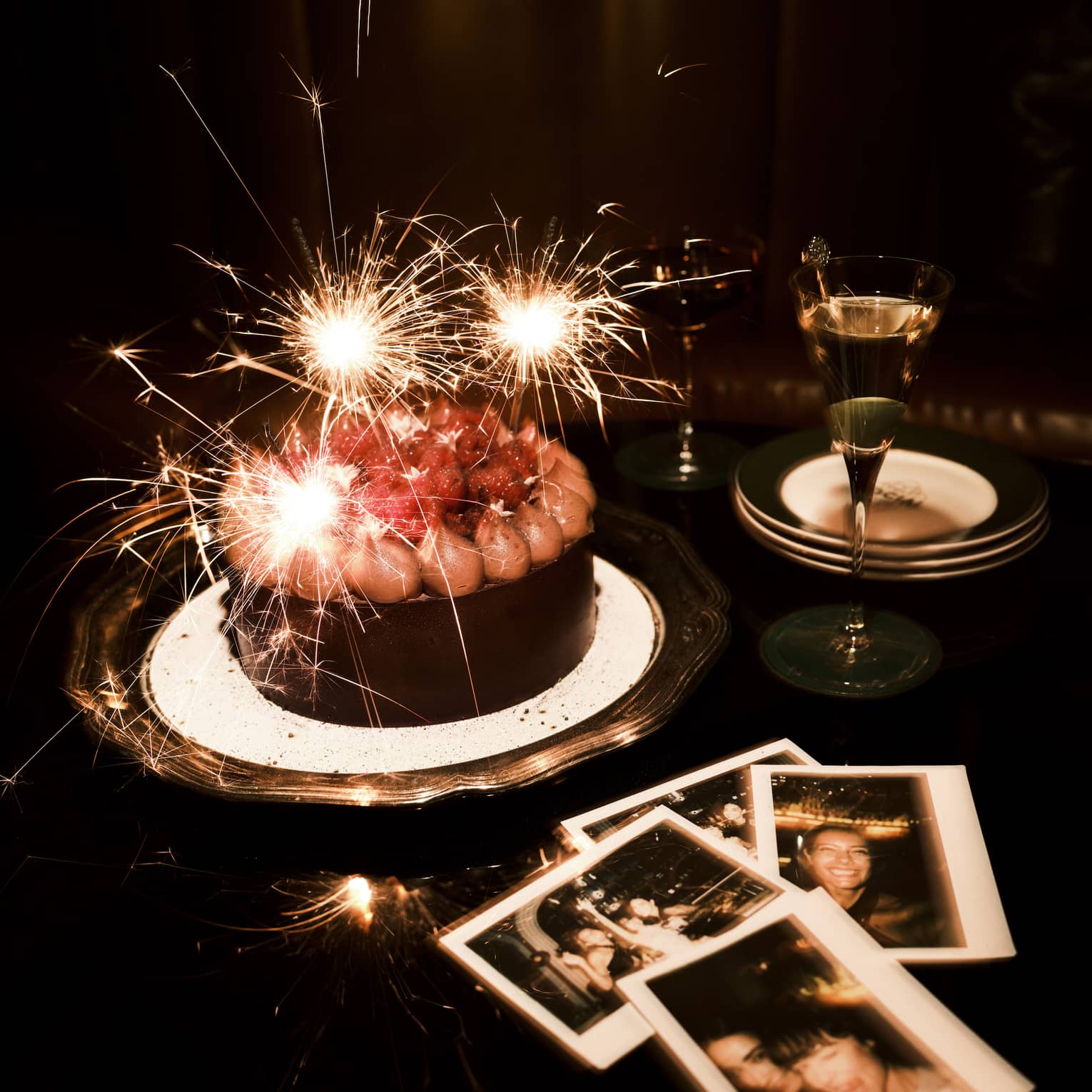 Sparkler candles in a chocolate cake and polaroid pictures nearby on a table