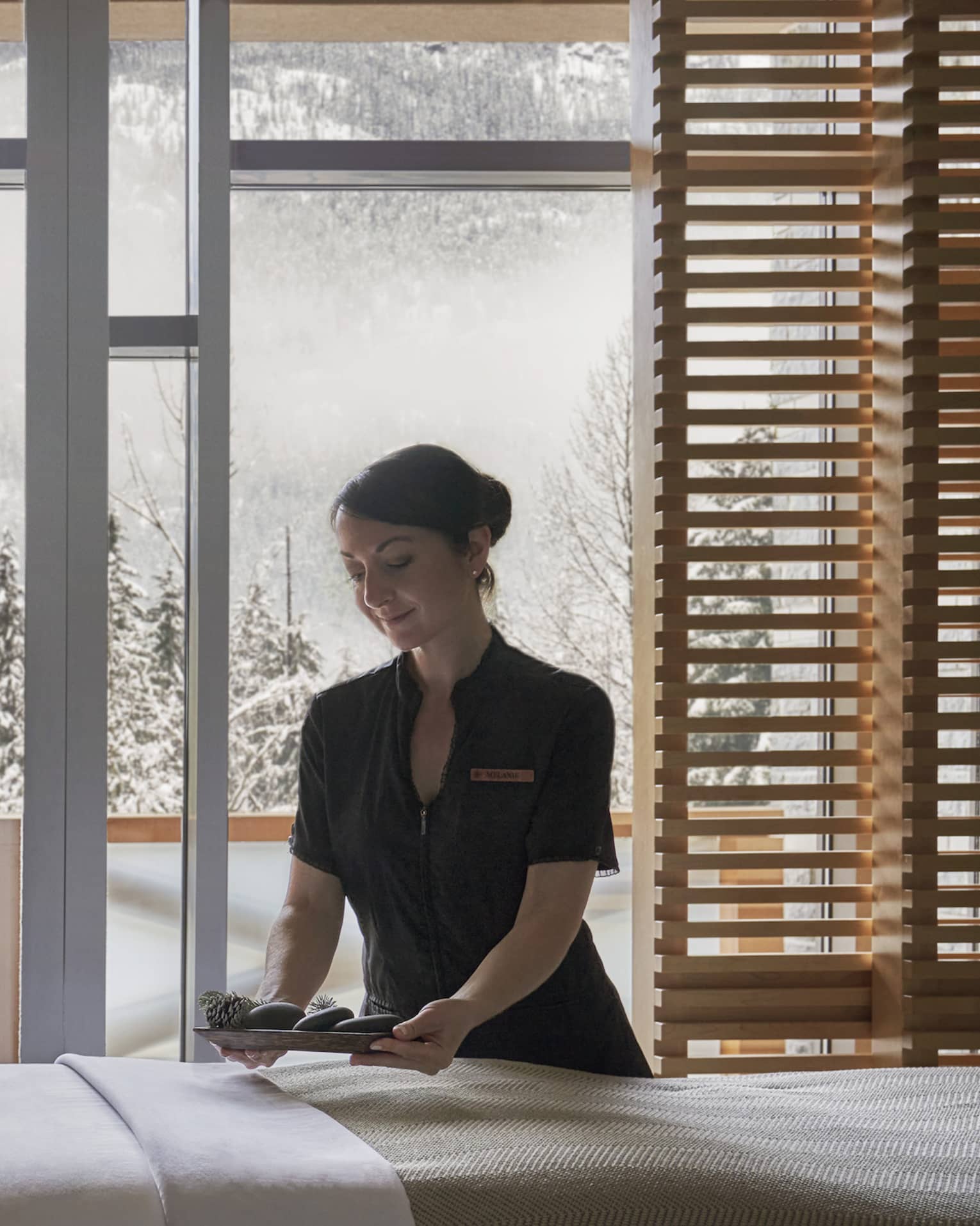 Spa staff smooths sheet on massage table in front of window with winter view