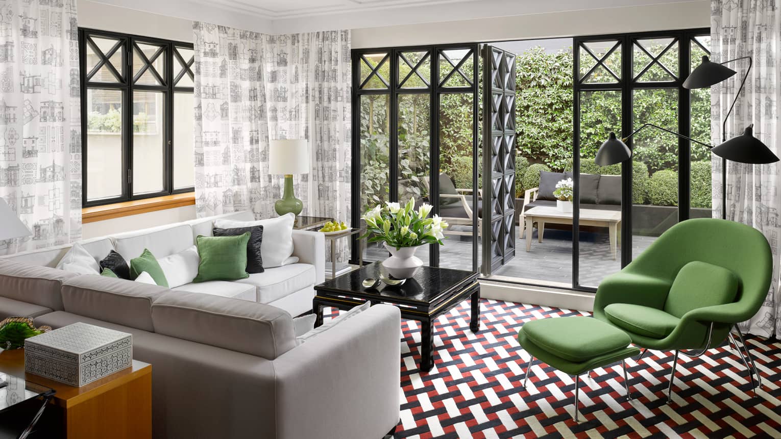 Fashion suite with terrace, featuring modern decor, a white sectional sofa, green accent chair, black and white patterned rug, and large windows leading to a private outdoor terrace.